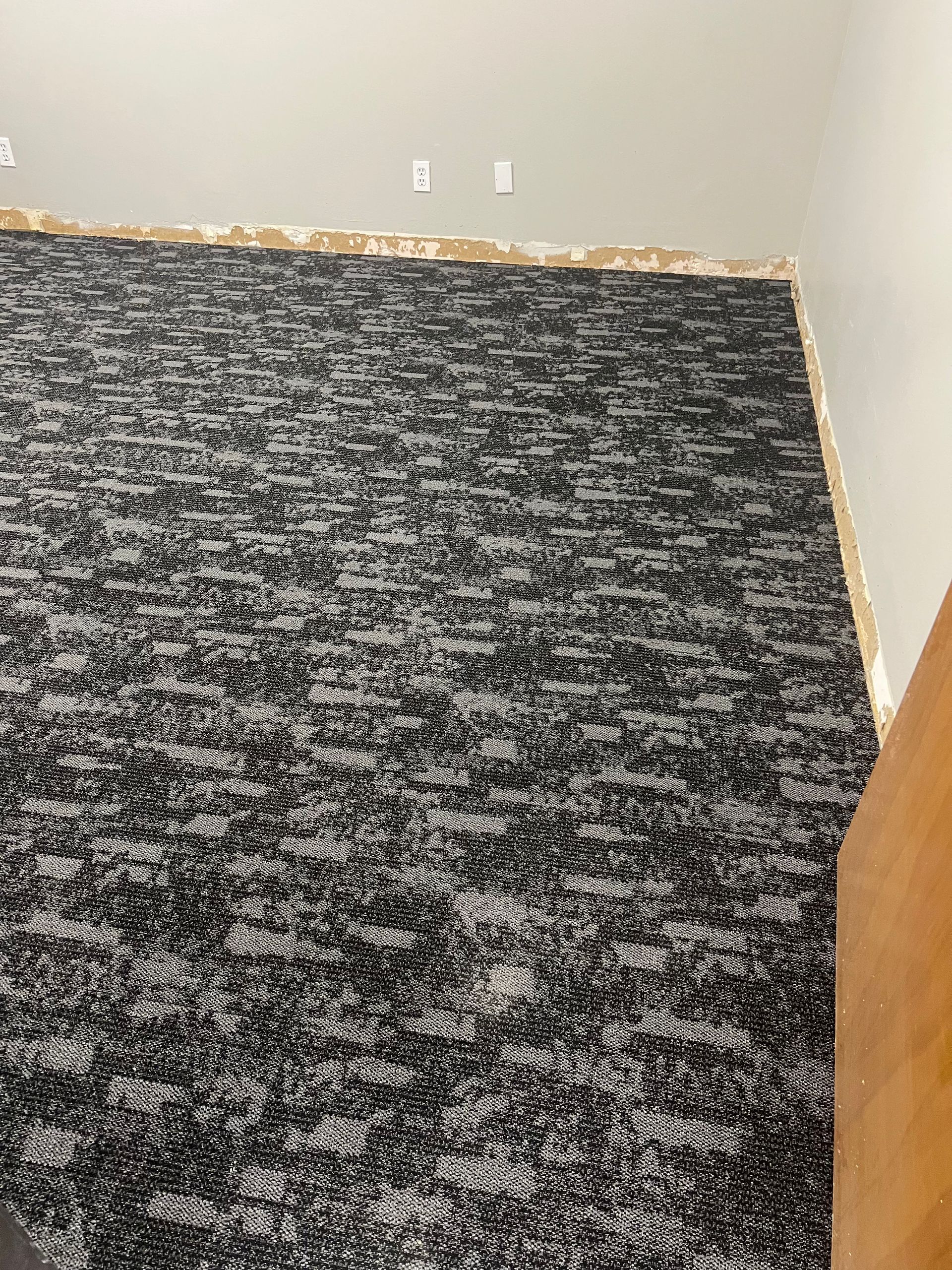 Black and gray patterned carpeted wall, top edge with exposed raw wood.