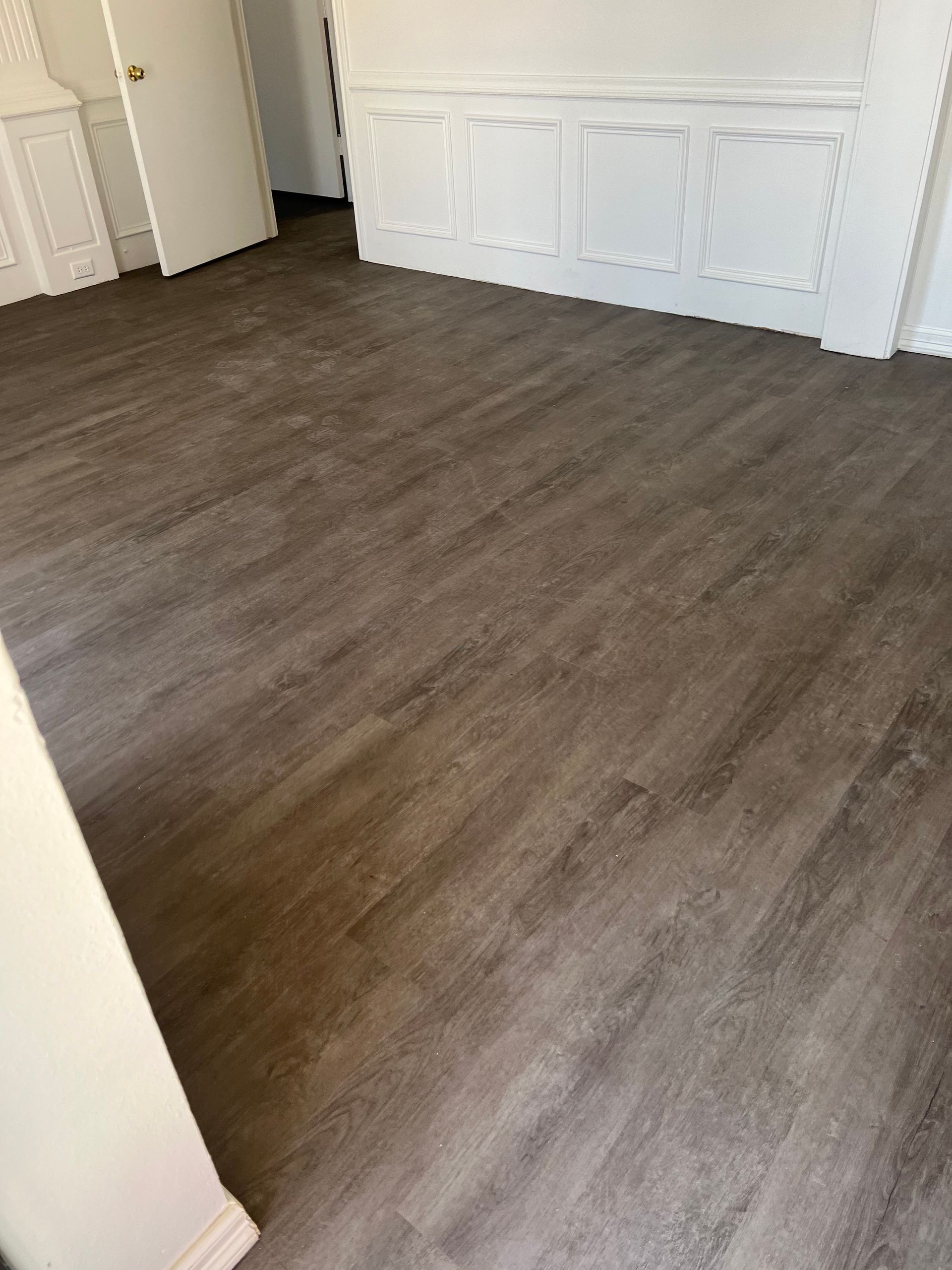 Dark wood-look flooring in a room with white walls and a door.