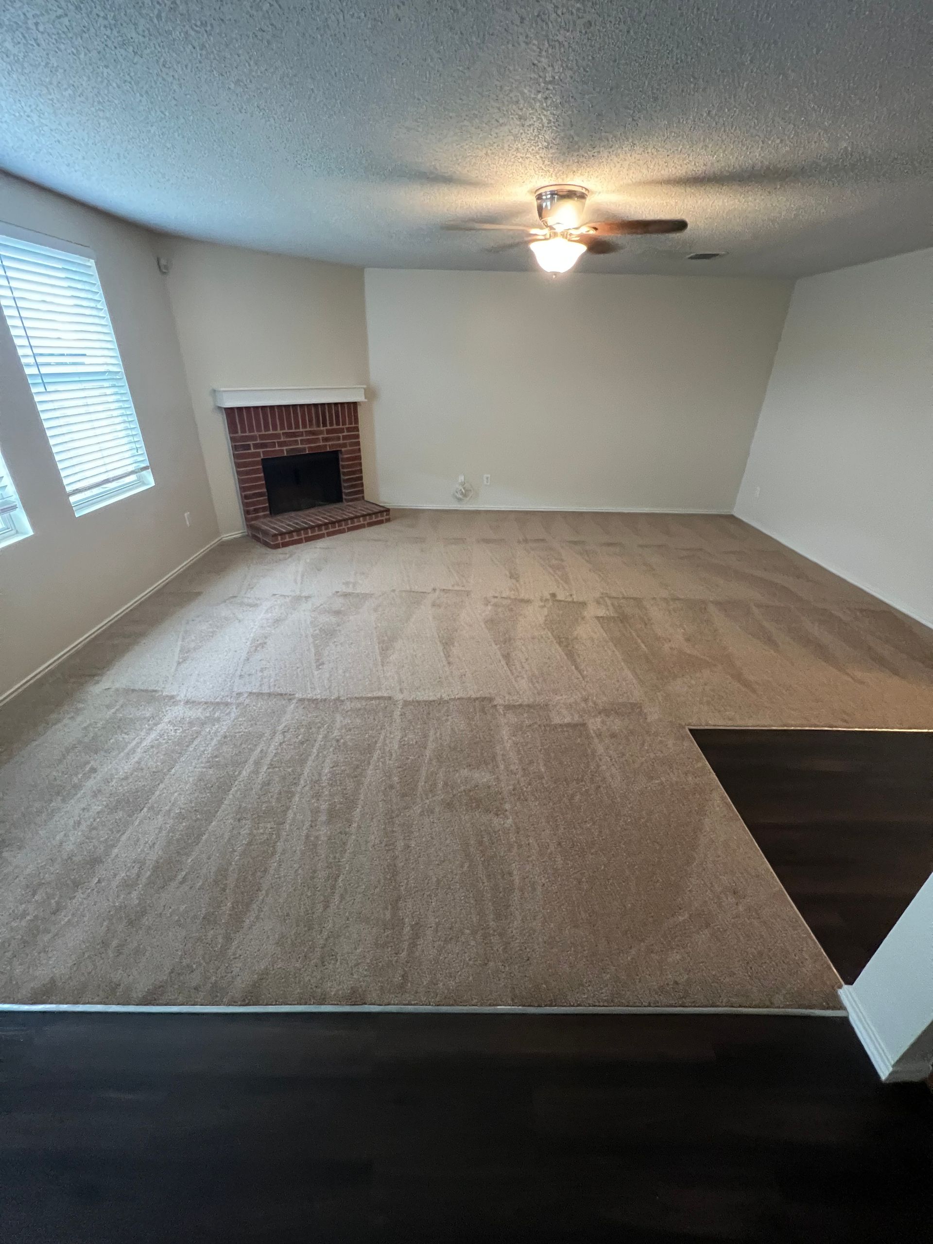 Empty living room with beige carpet, brick fireplace, and dark hardwood floor.