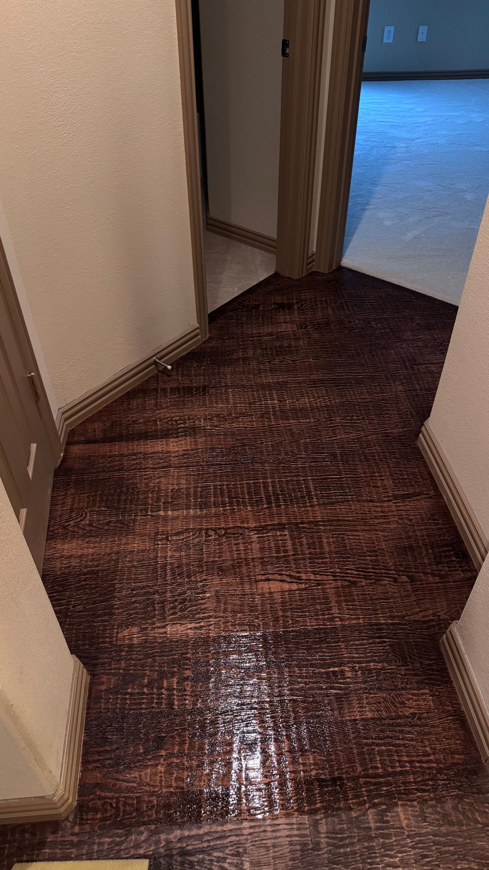 Hallway with brown tiled floor, doors, and a glimpse of carpeted room.