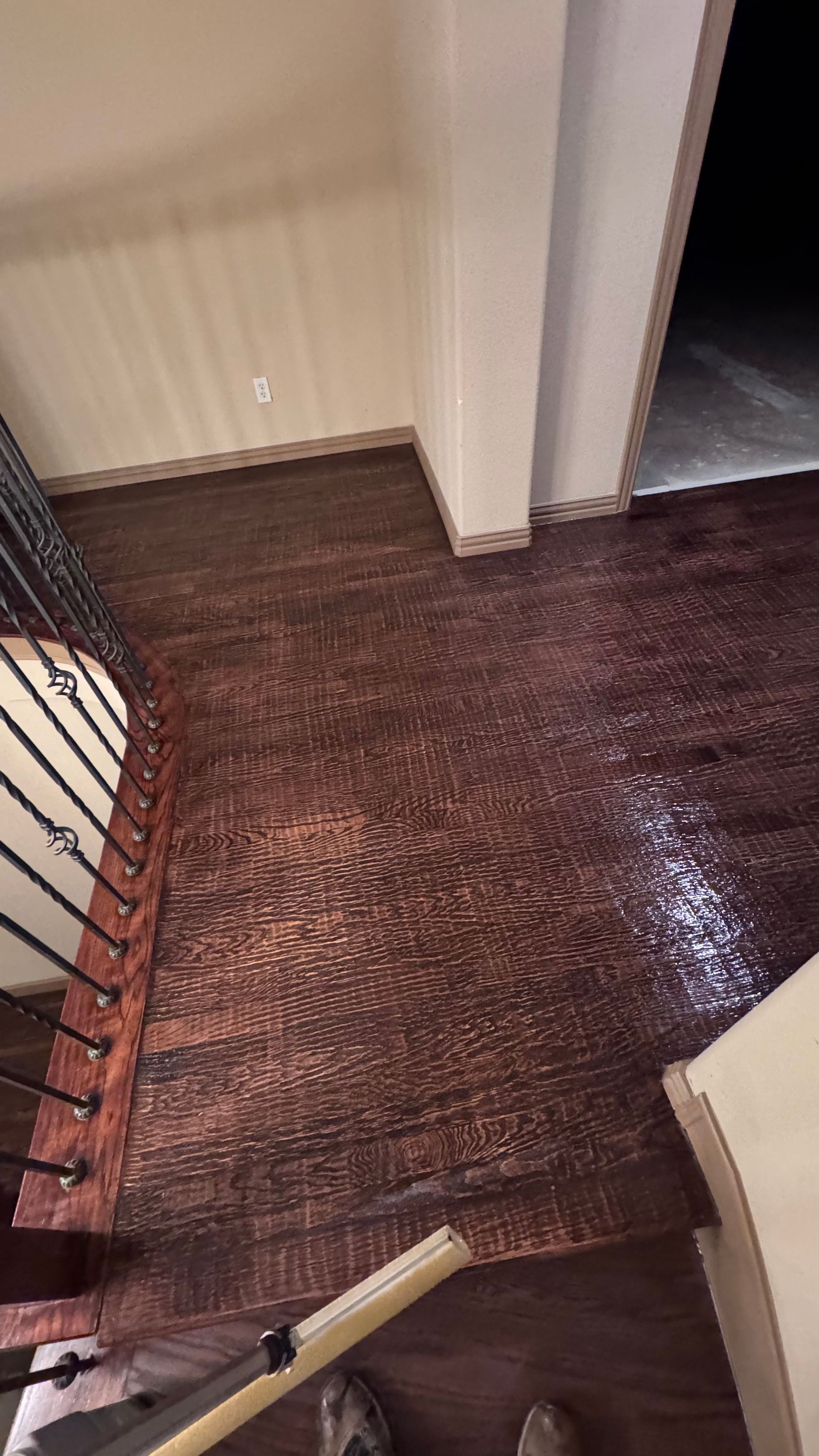 Wooden floor with stairwell, handrail, doorway; brown, dark, reflective.