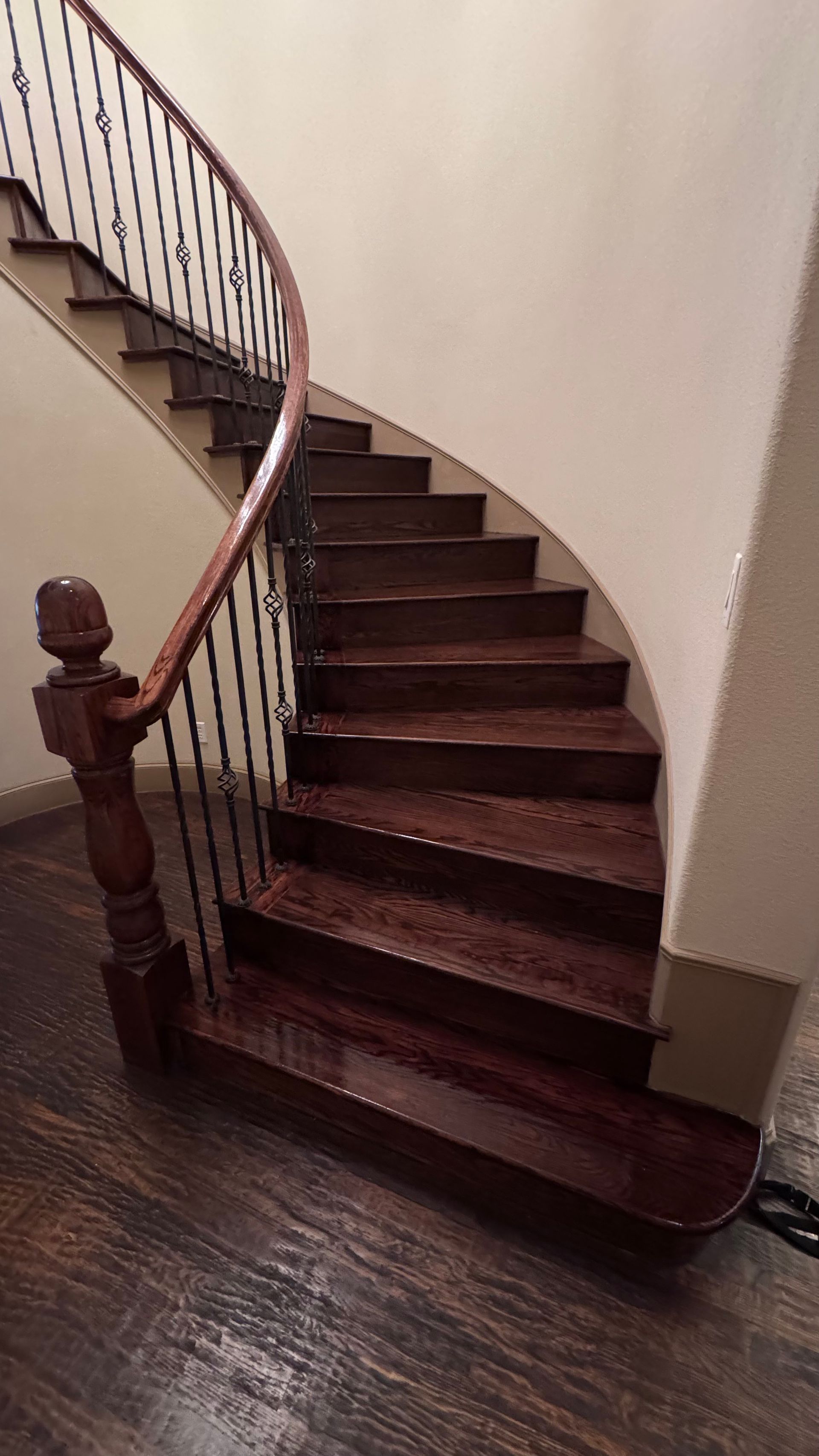 Wooden spiral staircase with dark wood treads, brown railing, and wrought iron balusters.