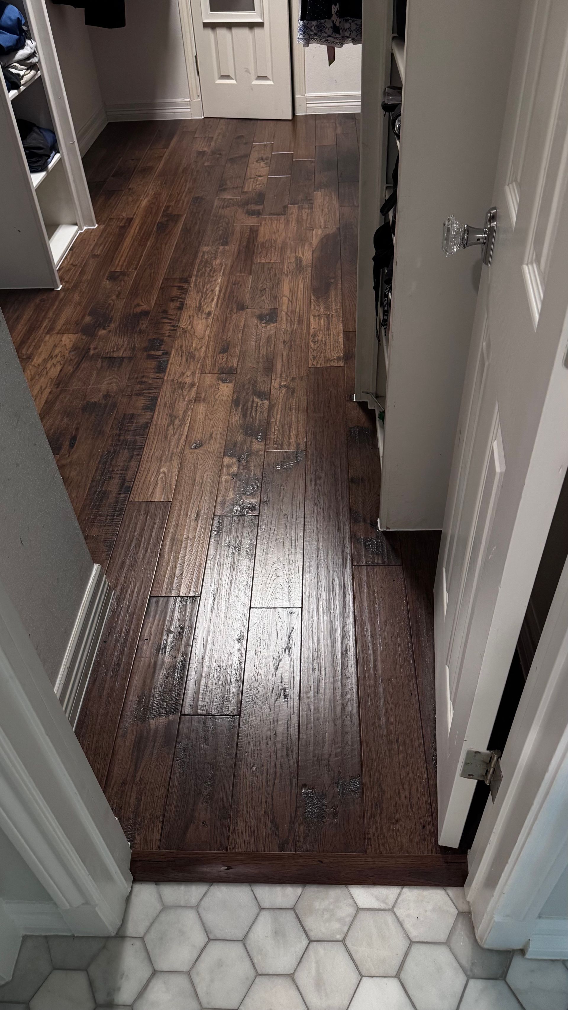 Dark wood floor hallway, leading to a white door. Hexagonal tile floor visible in the foreground.