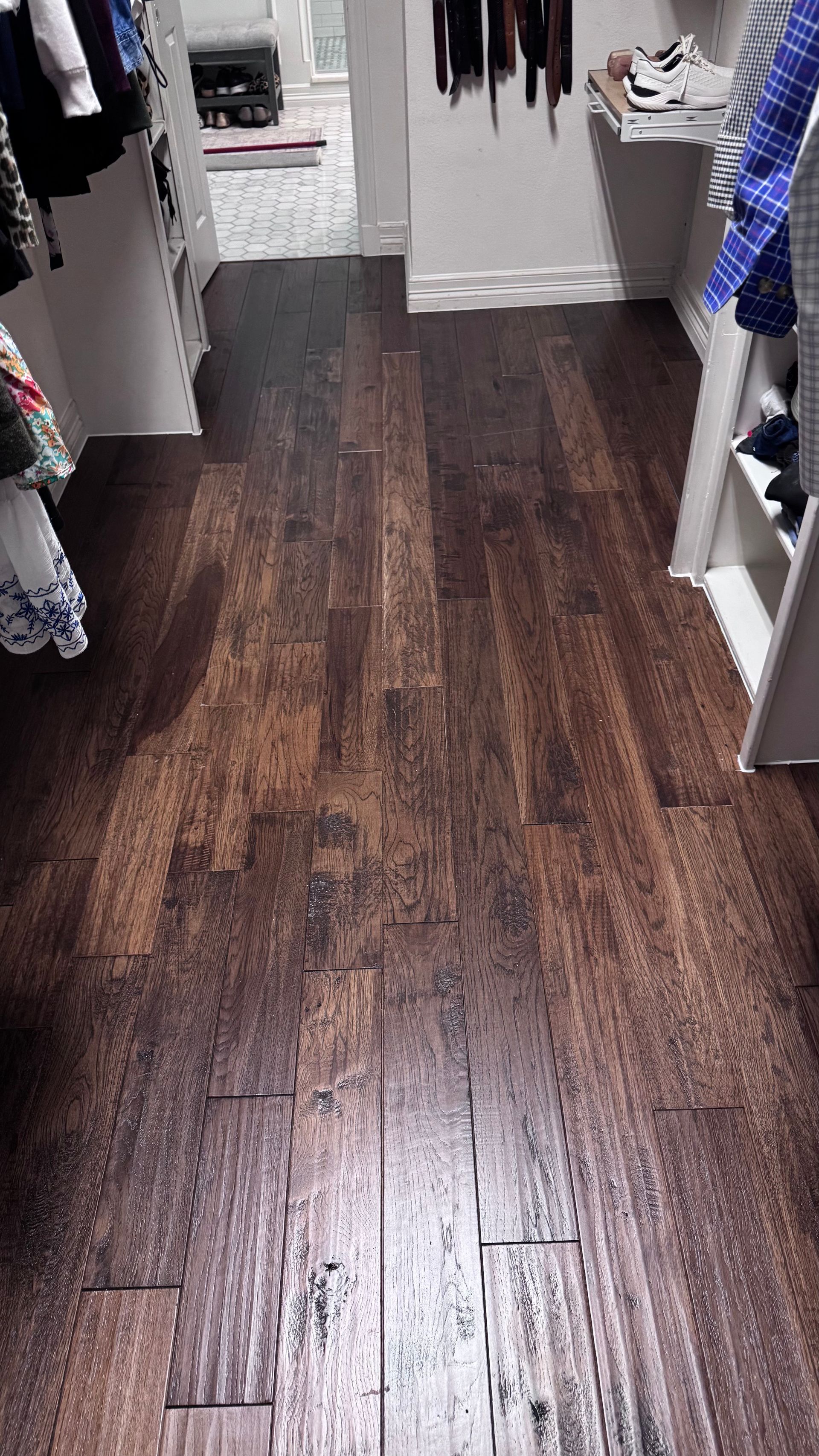 Dark hardwood floor in a closet, with white shelving and racks of clothes on either side.