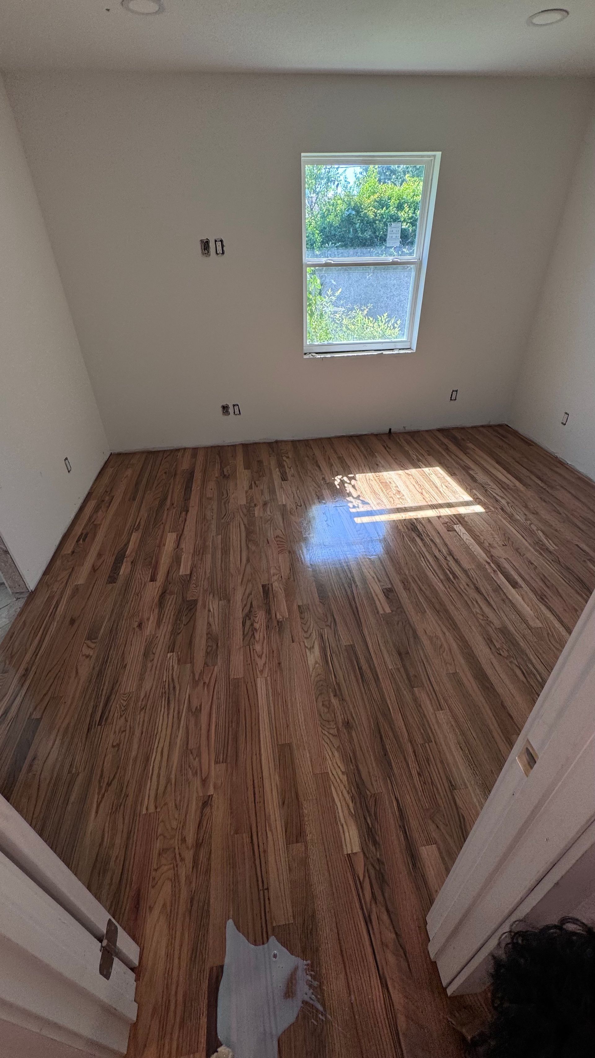 Hardwood floor in an attic room with a window. Sunlight reflects off the floor. The walls are white.