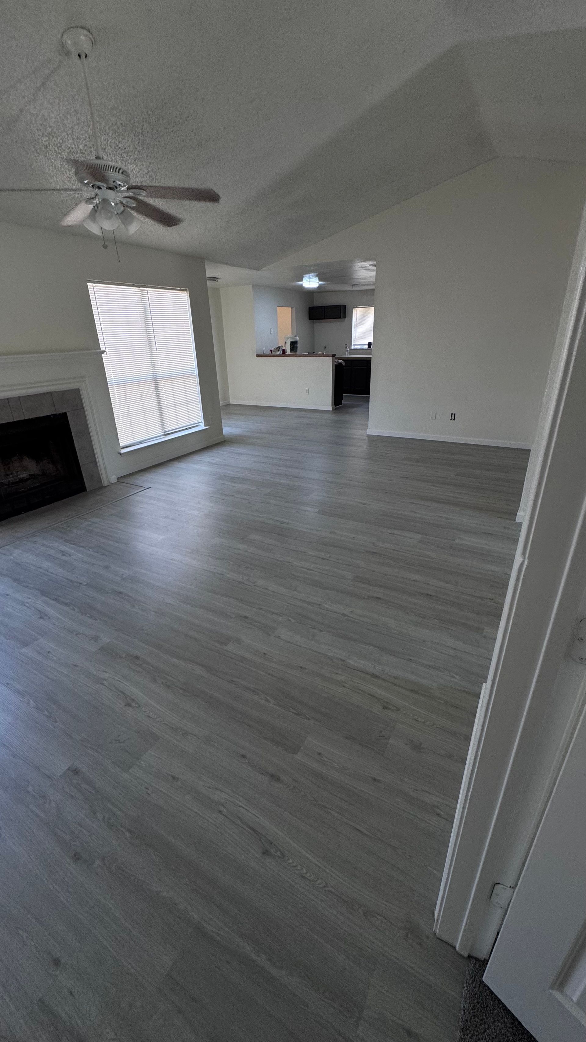 Living room with gray wood-look flooring, fireplace, and view of kitchen. White walls and ceiling.