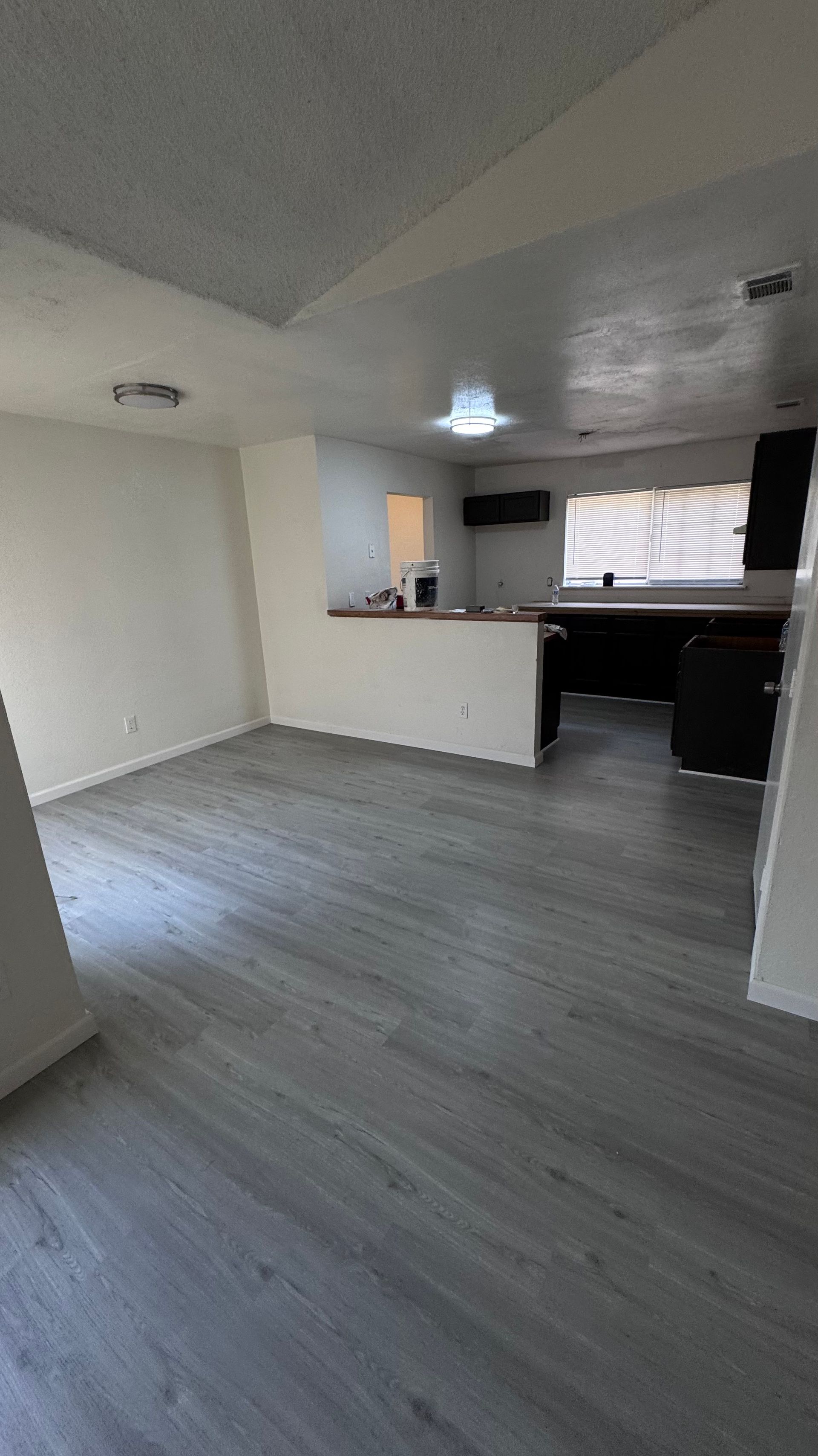 Empty living room with gray flooring, a short wall separating the kitchen area.