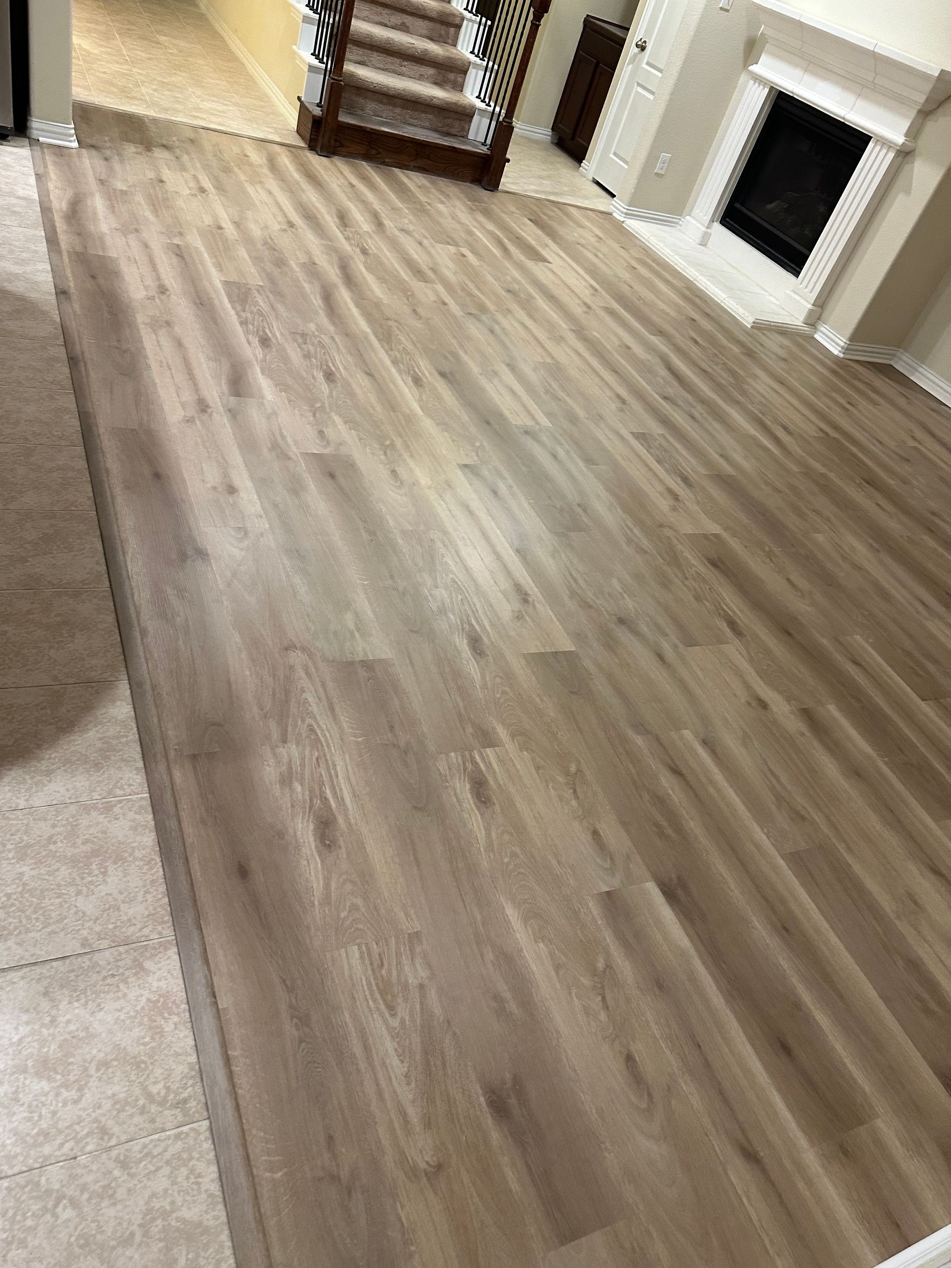 Light wood flooring in a living room, near a staircase and fireplace.