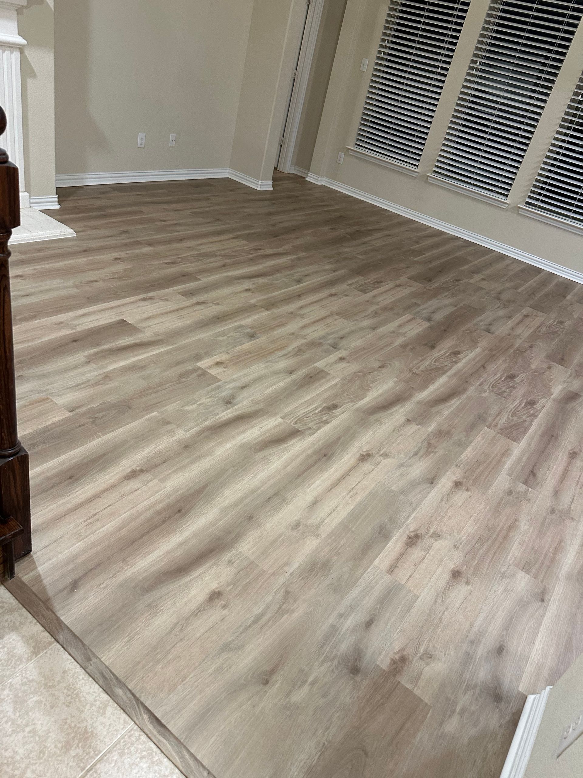Light brown wood-look flooring in a room with white trim and a window with blinds.