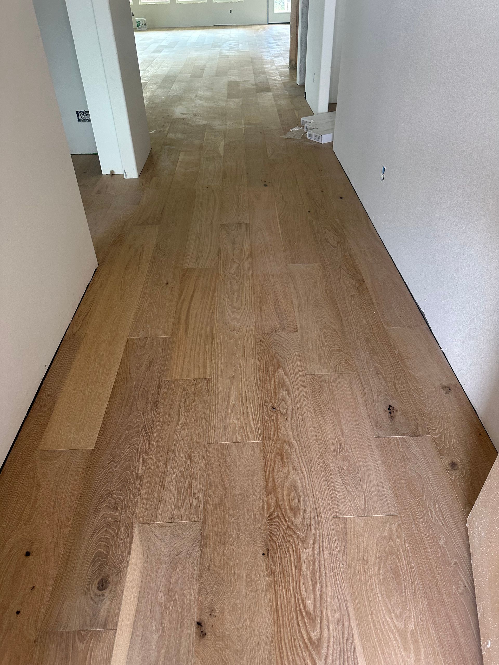 Light brown hardwood flooring in a hallway, partially installed, with white walls.