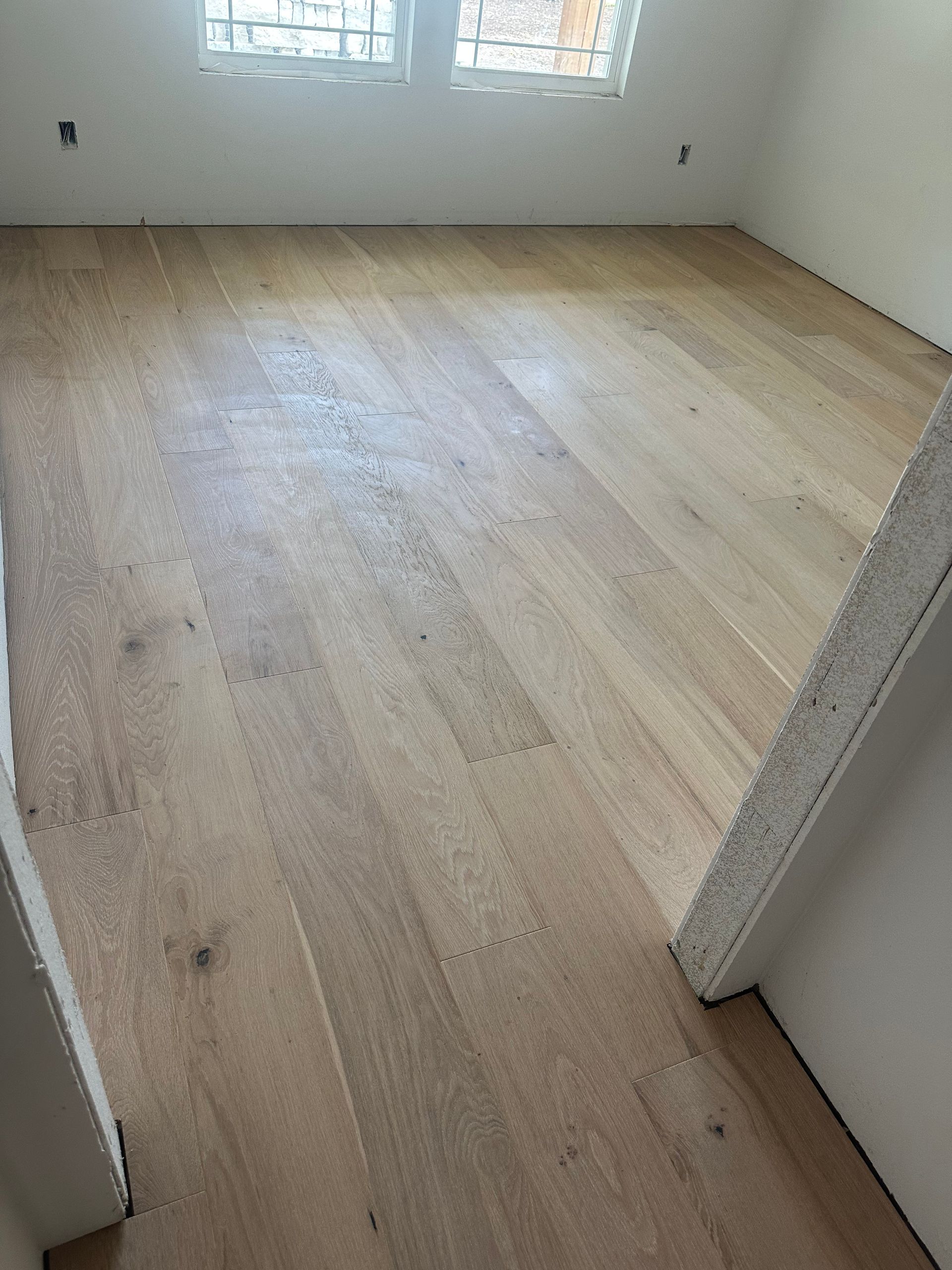 Light-colored hardwood floor in a room with white walls and a window.