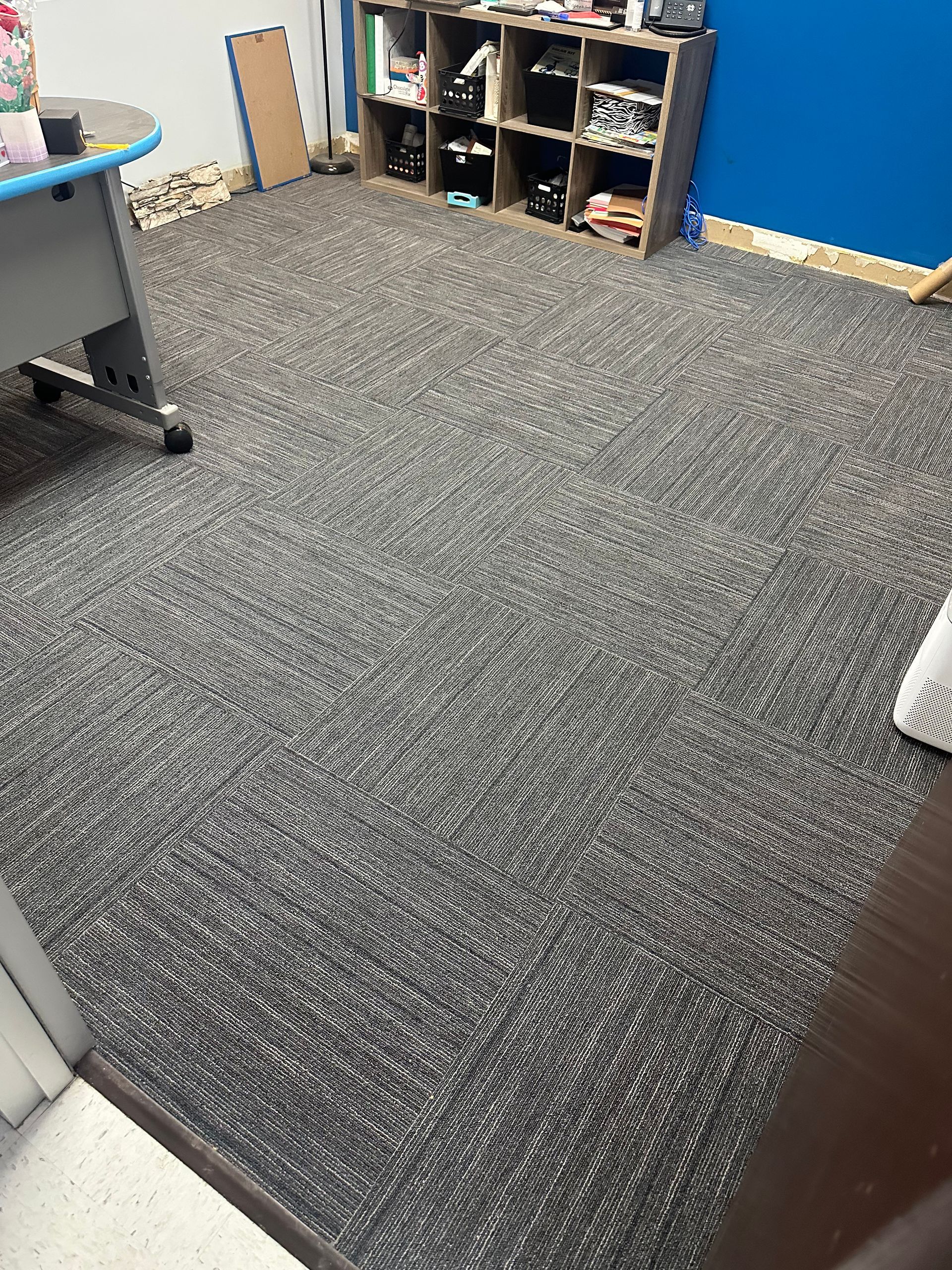 A room with gray and black swirled carpet and wood shelving filled with items against a blue wall.