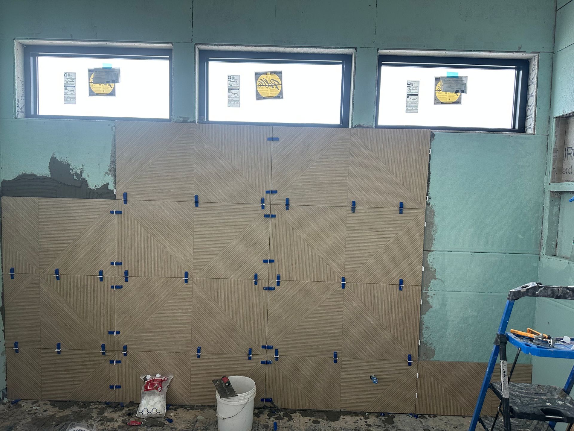 Bathroom wall with tan patterned tiles being installed, blue spacers visible.
