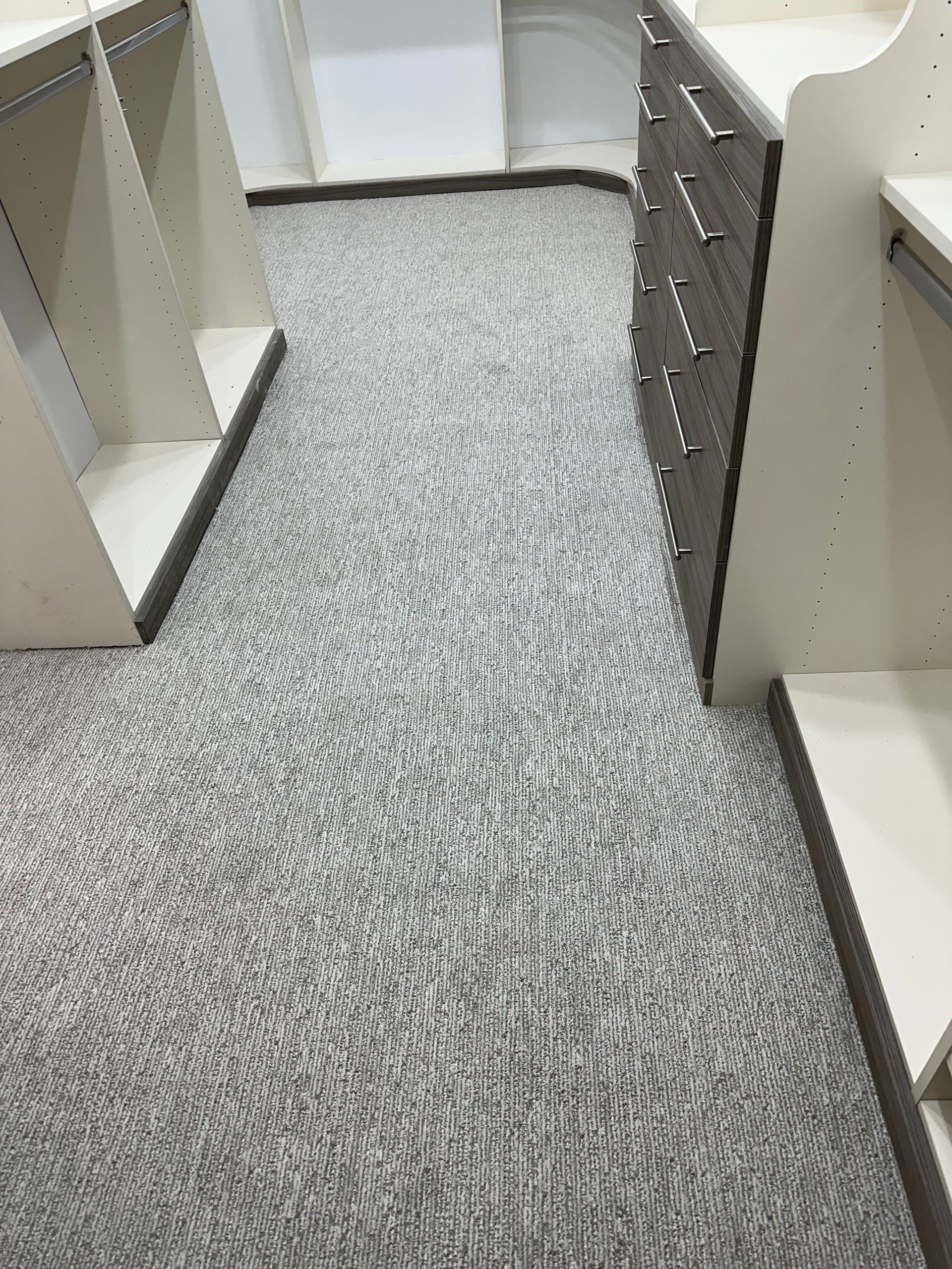 Closet with gray patterned carpet, white shelves, and a chest of drawers with silver handles.