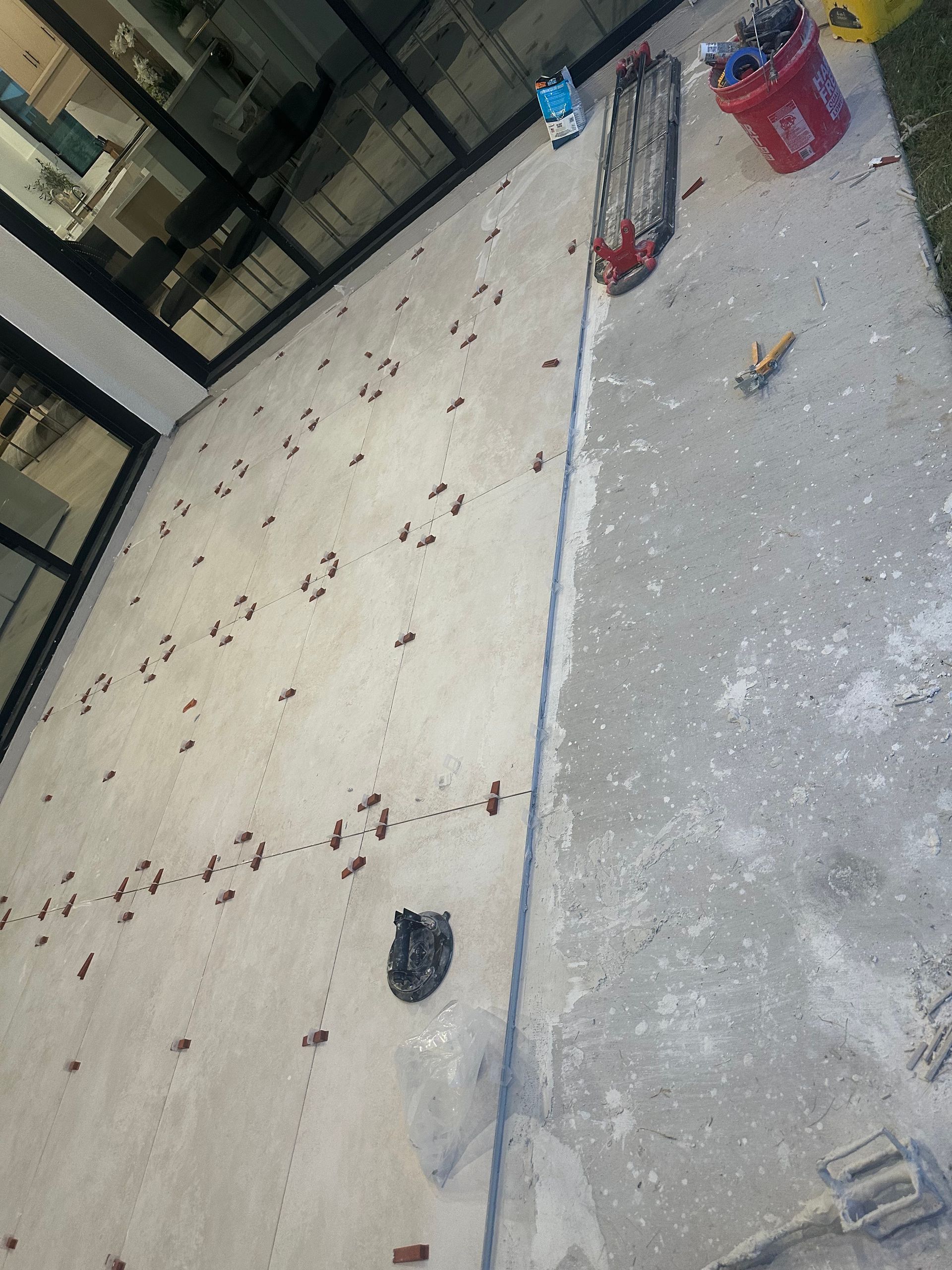 Concrete wall with debris; tools and bucket at the top, near a building with large windows.