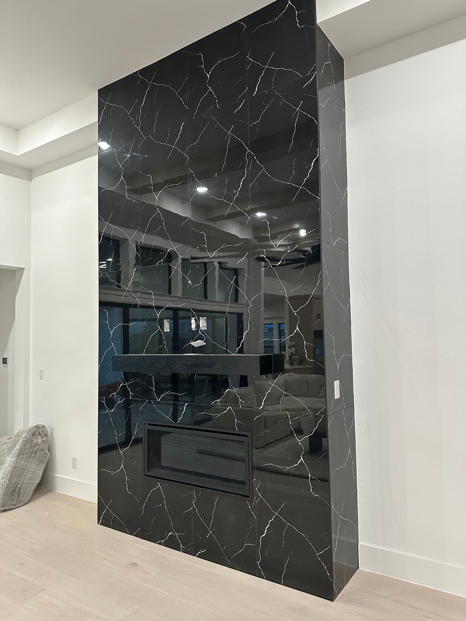 Black, vertically-oriented fireplace with white veining; set between white walls and light wood floor.