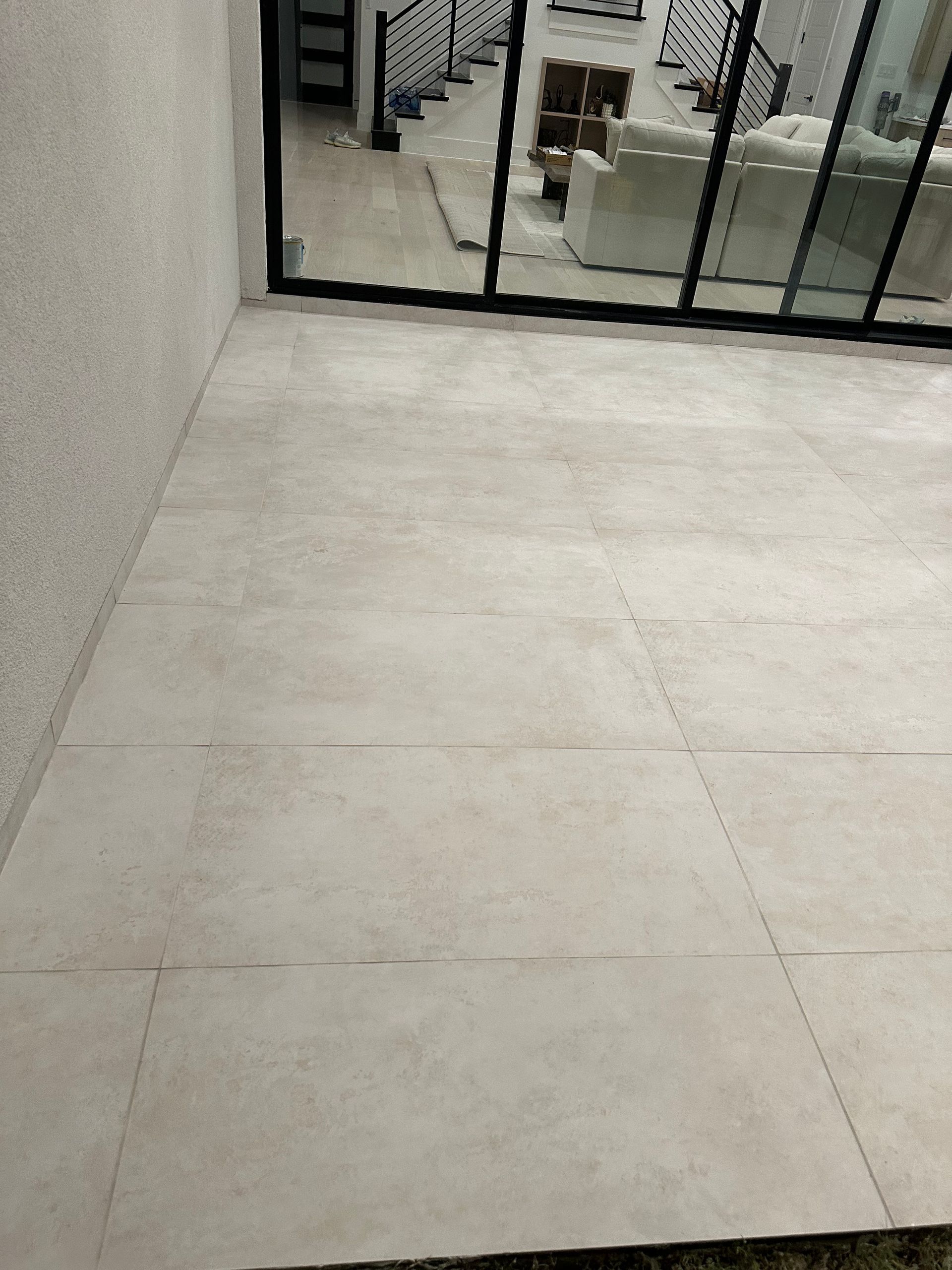 Gray tiled floor next to a textured wall and glass doors leading to a living area with white furniture.