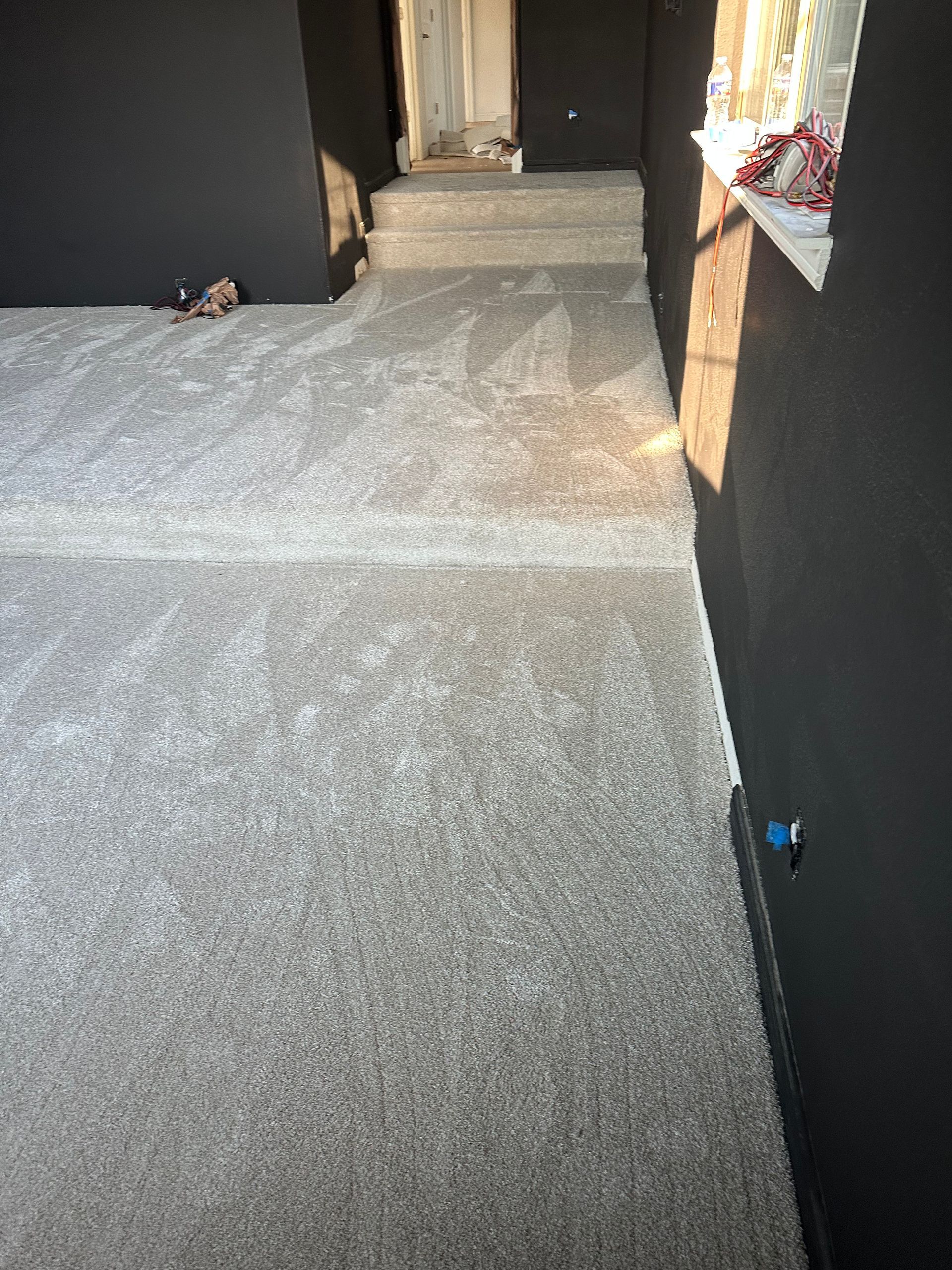 Gray textured floor with dark gray walls, leading to a doorway. Sunlight enters through a window.