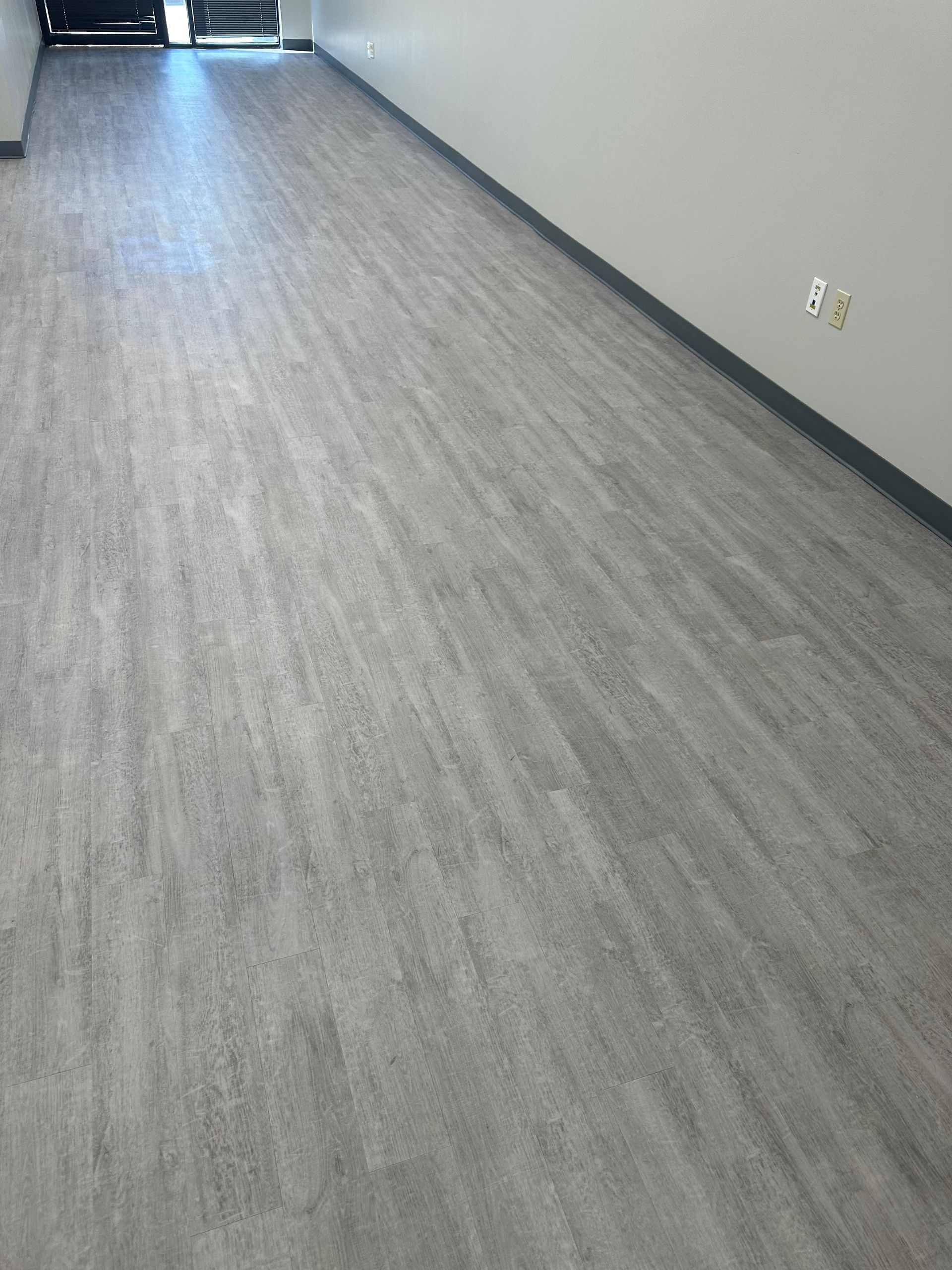 Empty room with gray wood-look flooring, white walls, and dark baseboards.