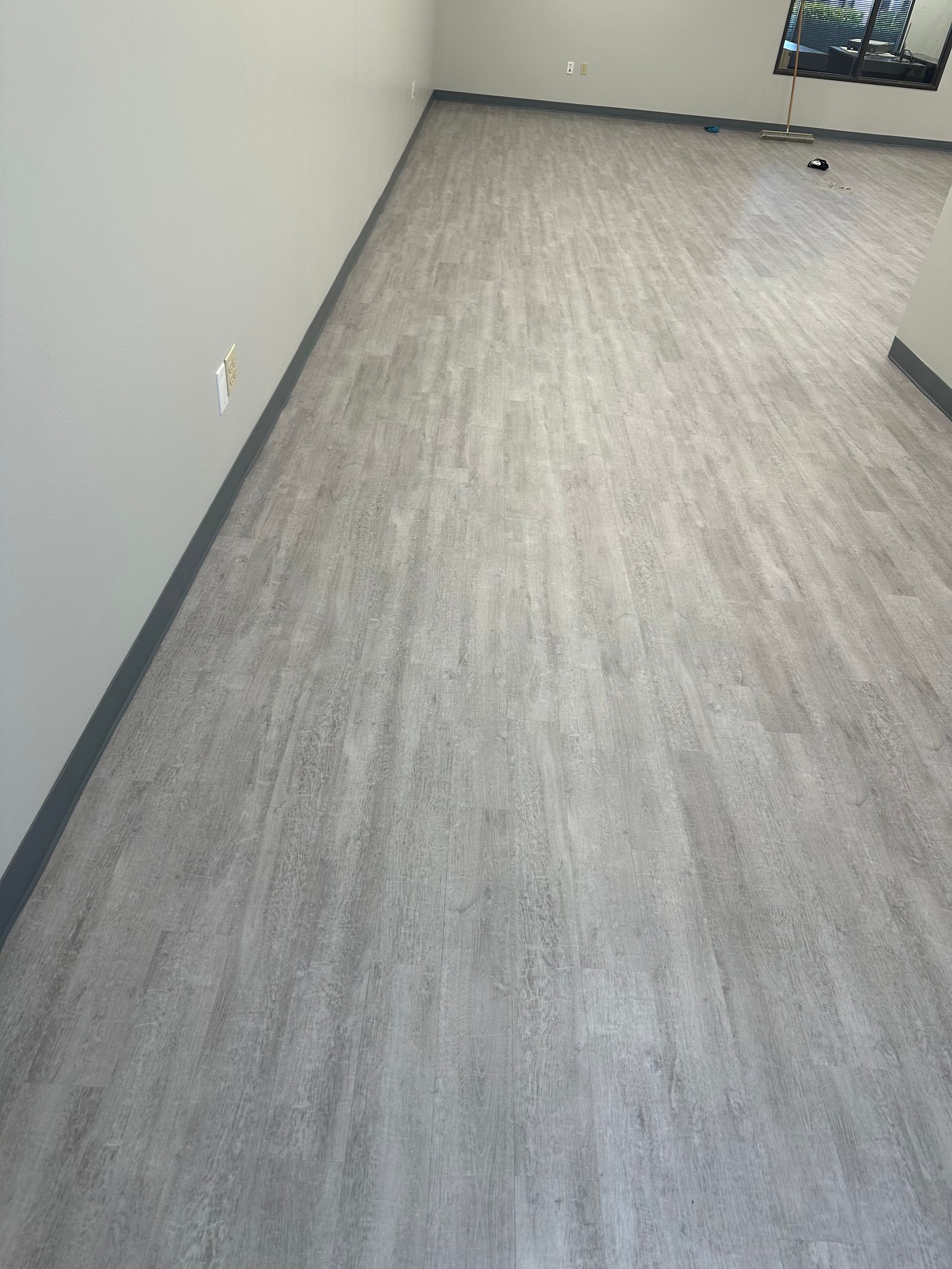 Grey vinyl flooring installed in a room, baseboards along the wall.