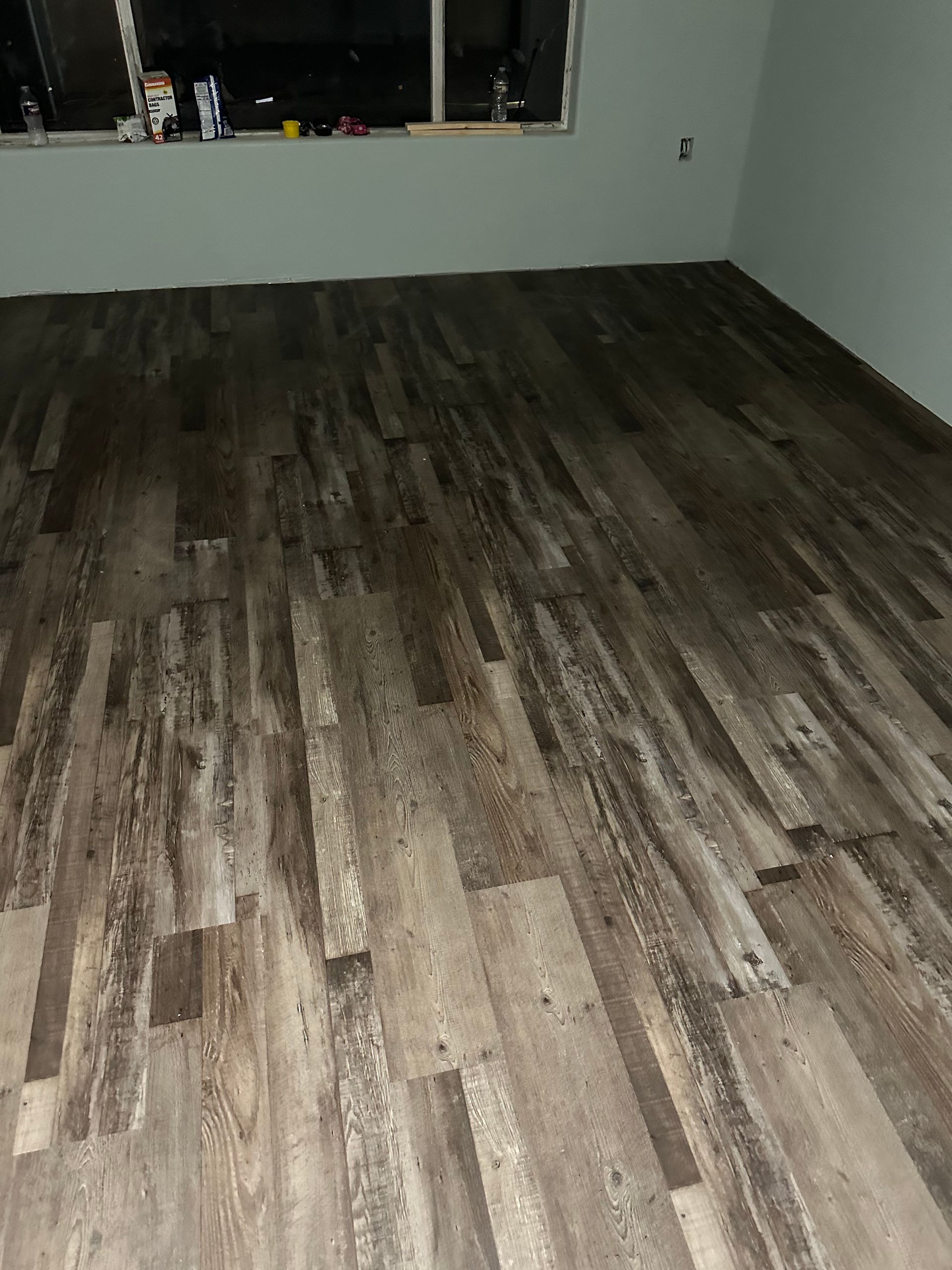Dark wood-look flooring in a room with light green walls and a window.