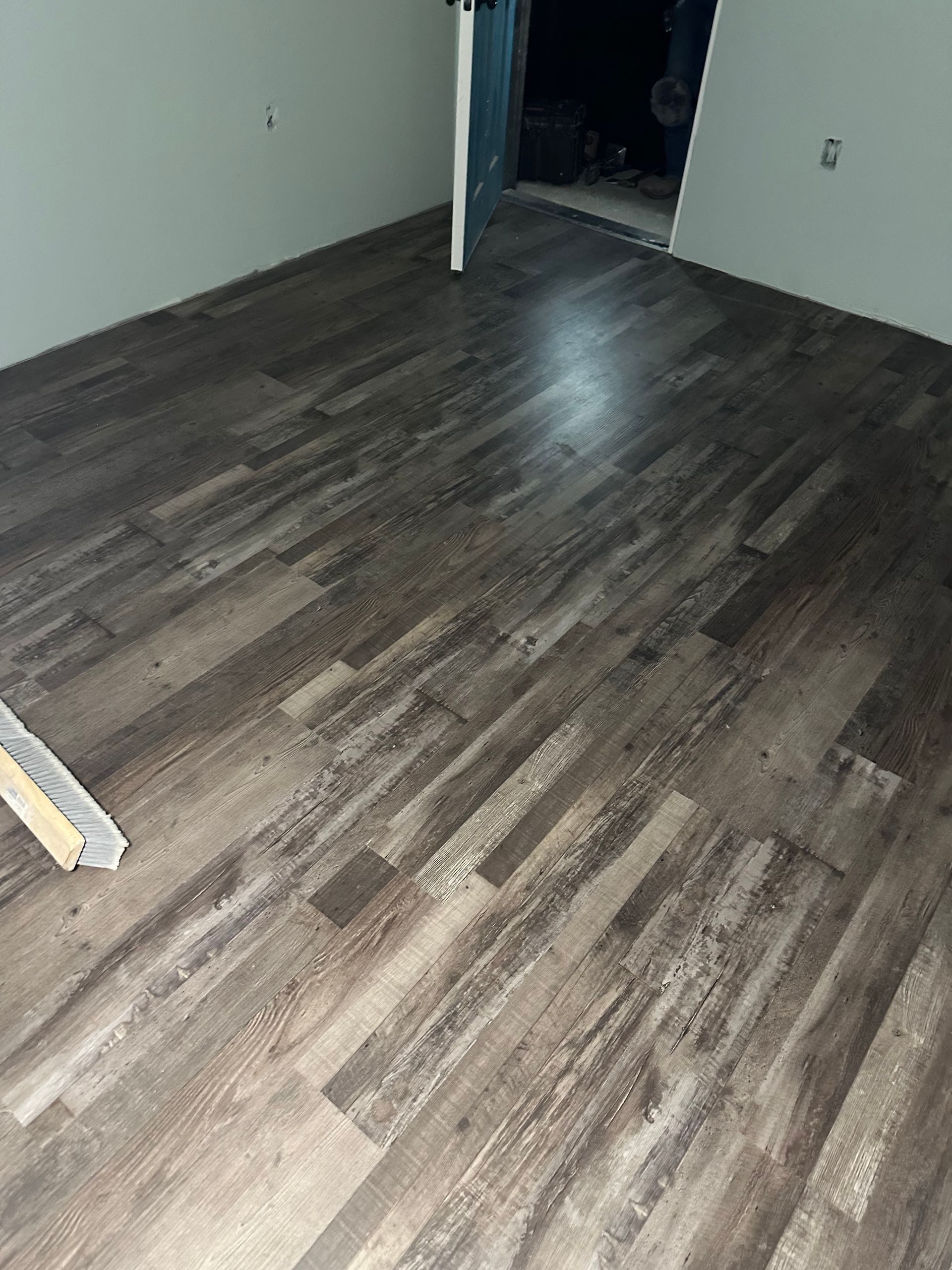 Newly installed wood-look laminate flooring in a room with light-colored walls and a doorway in the background.