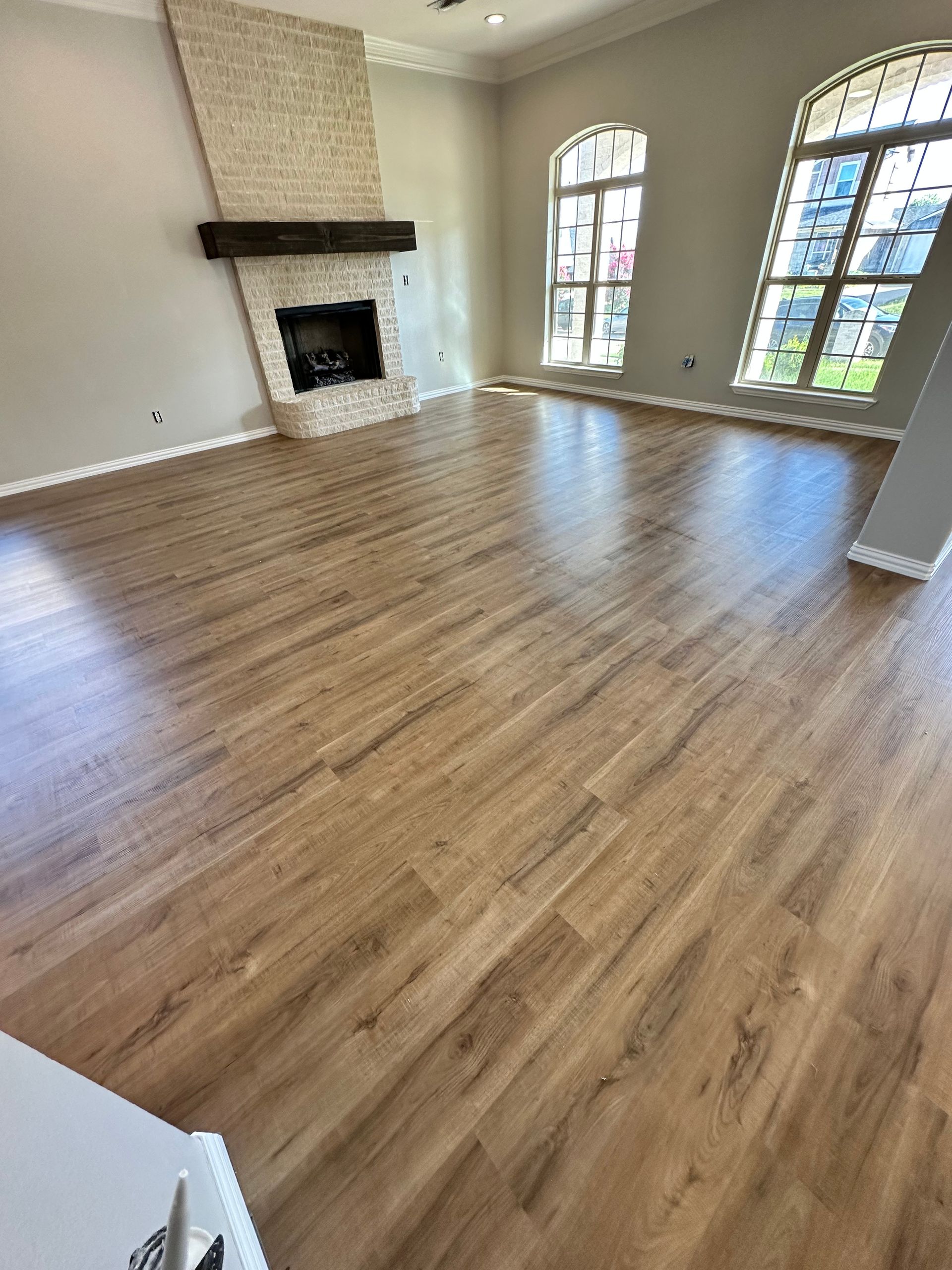 Spacious room with wood-look flooring, brick fireplace, arched windows, and neutral walls.