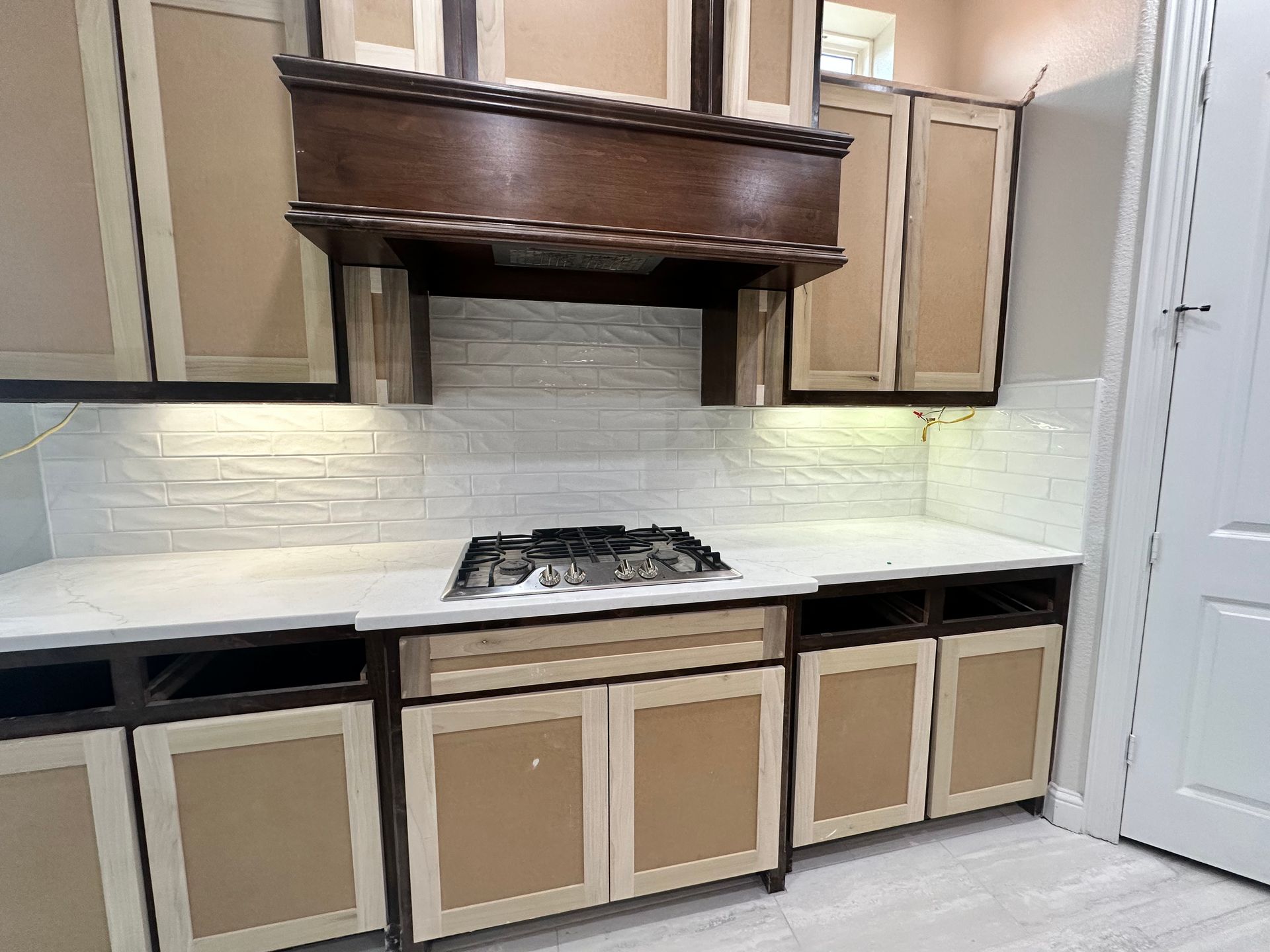 Kitchen with unfinished cabinets, range, and hood in a room with white walls.