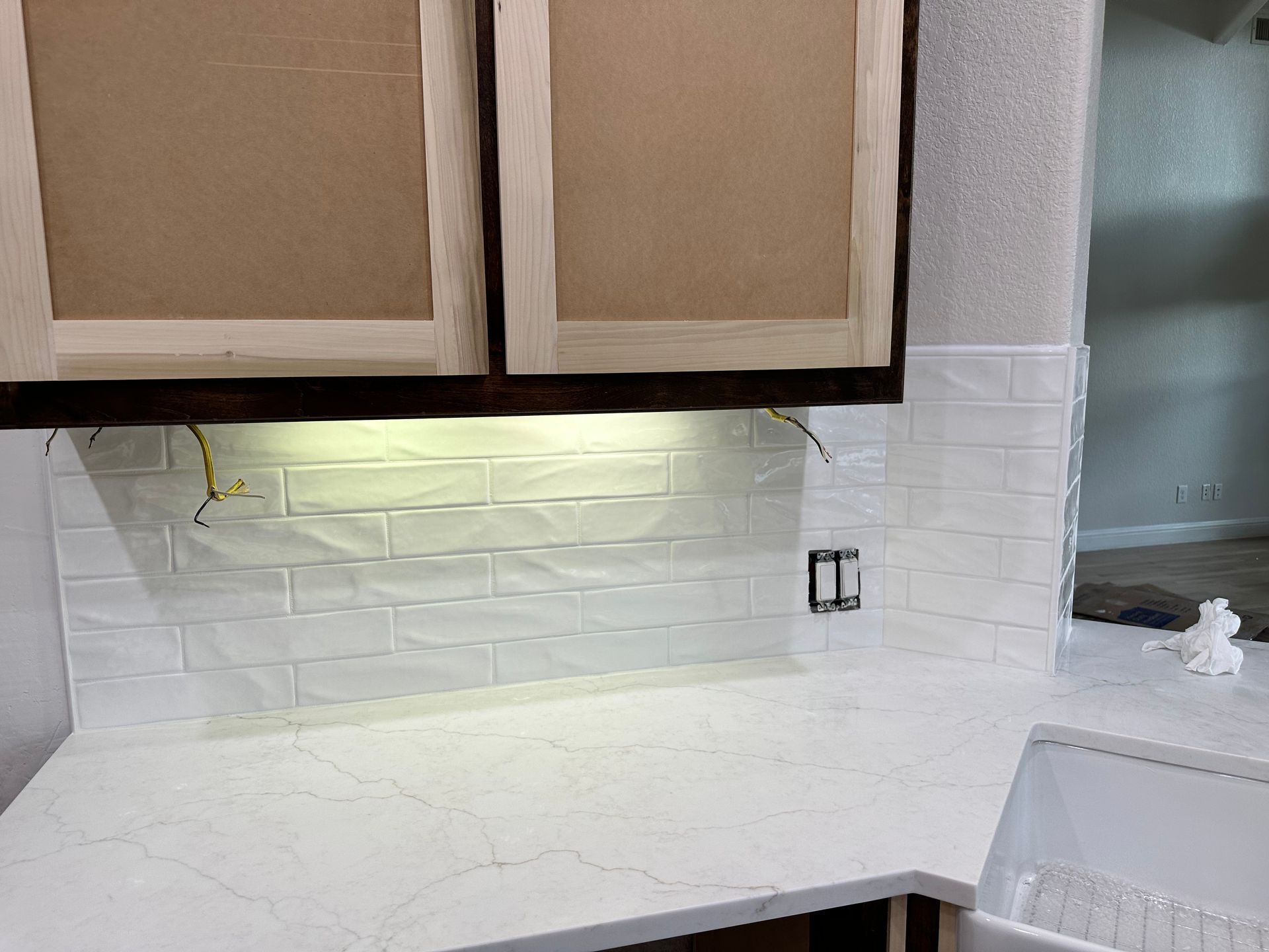 Kitchen under construction with white subway tile backsplash, white countertops, and upper cabinets.