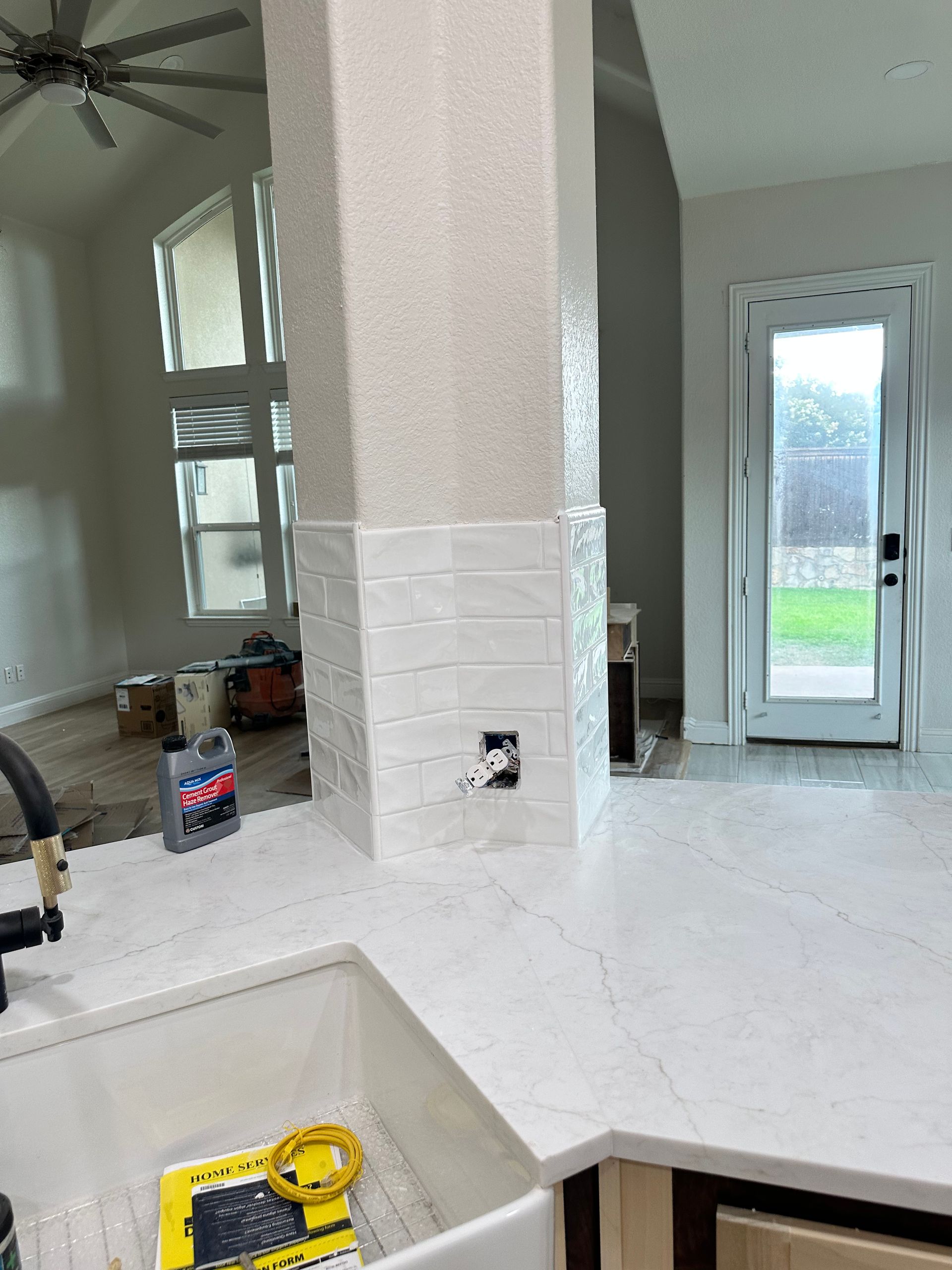 Kitchen renovation with white countertop, tiled pillar, and a view of a door to a yard.