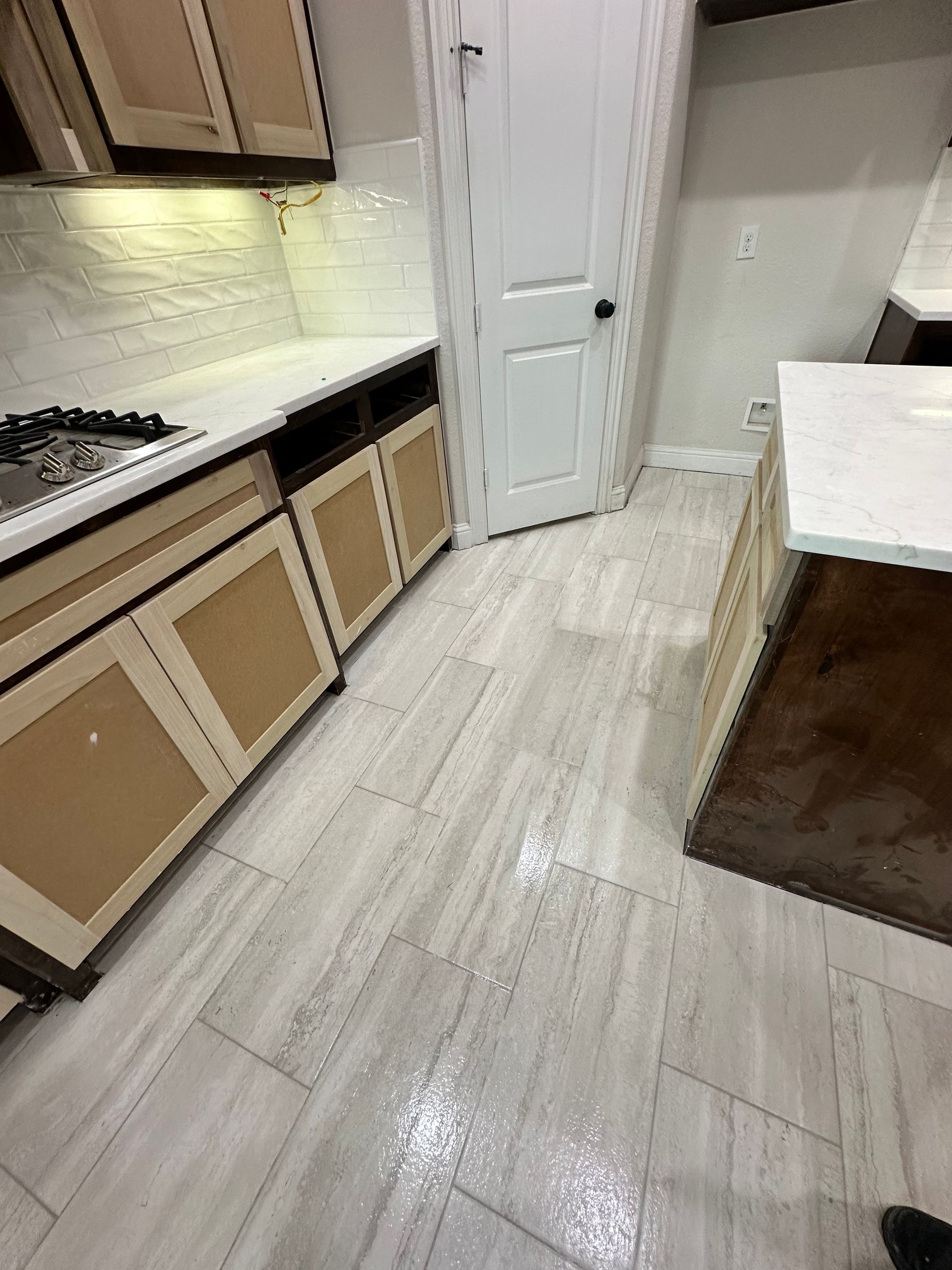 Kitchen with light wood cabinets, white countertops, and gray tile floor; white door in background.