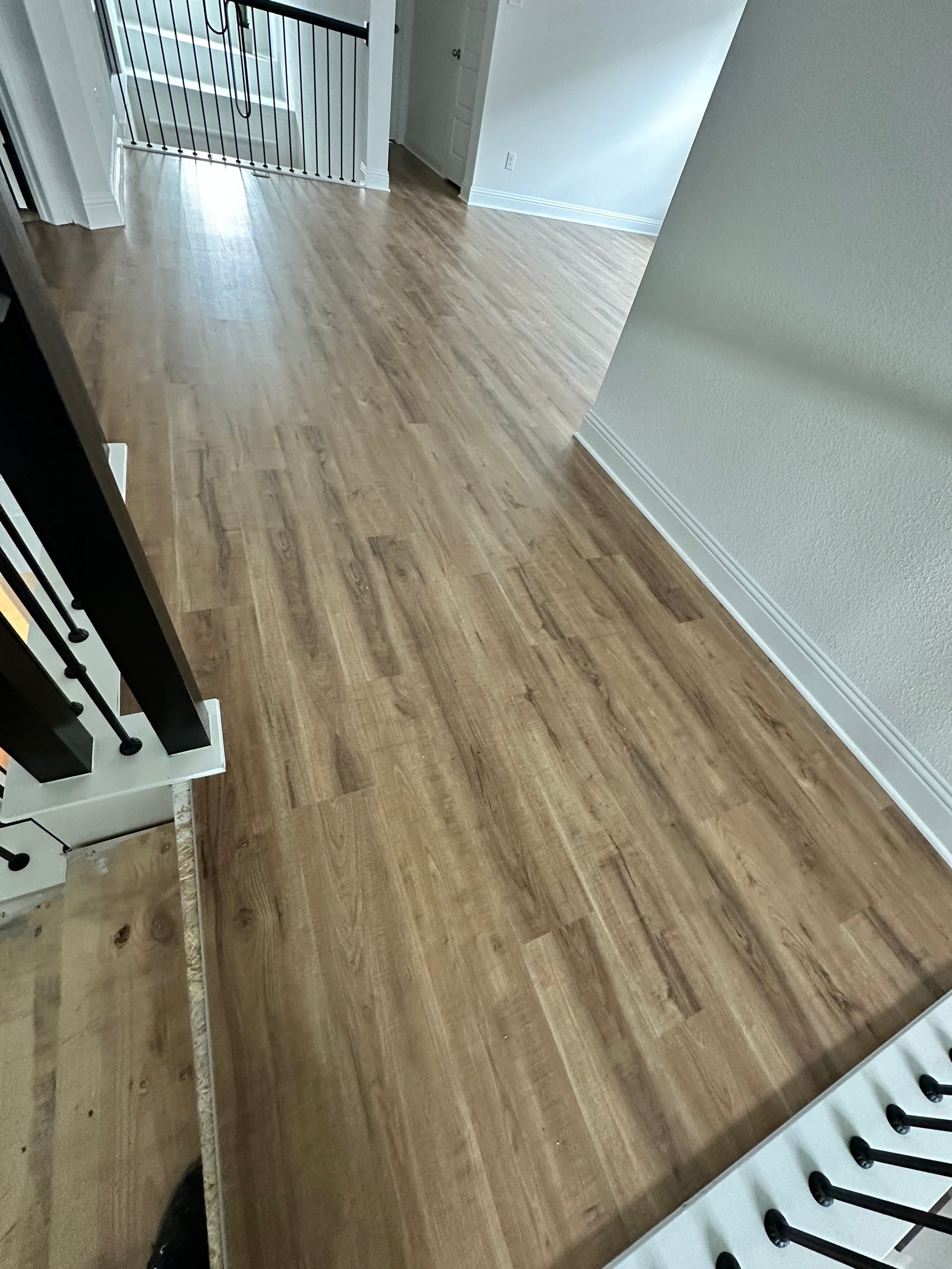 Wooden hallway with stairs, black and white railing, and white walls.