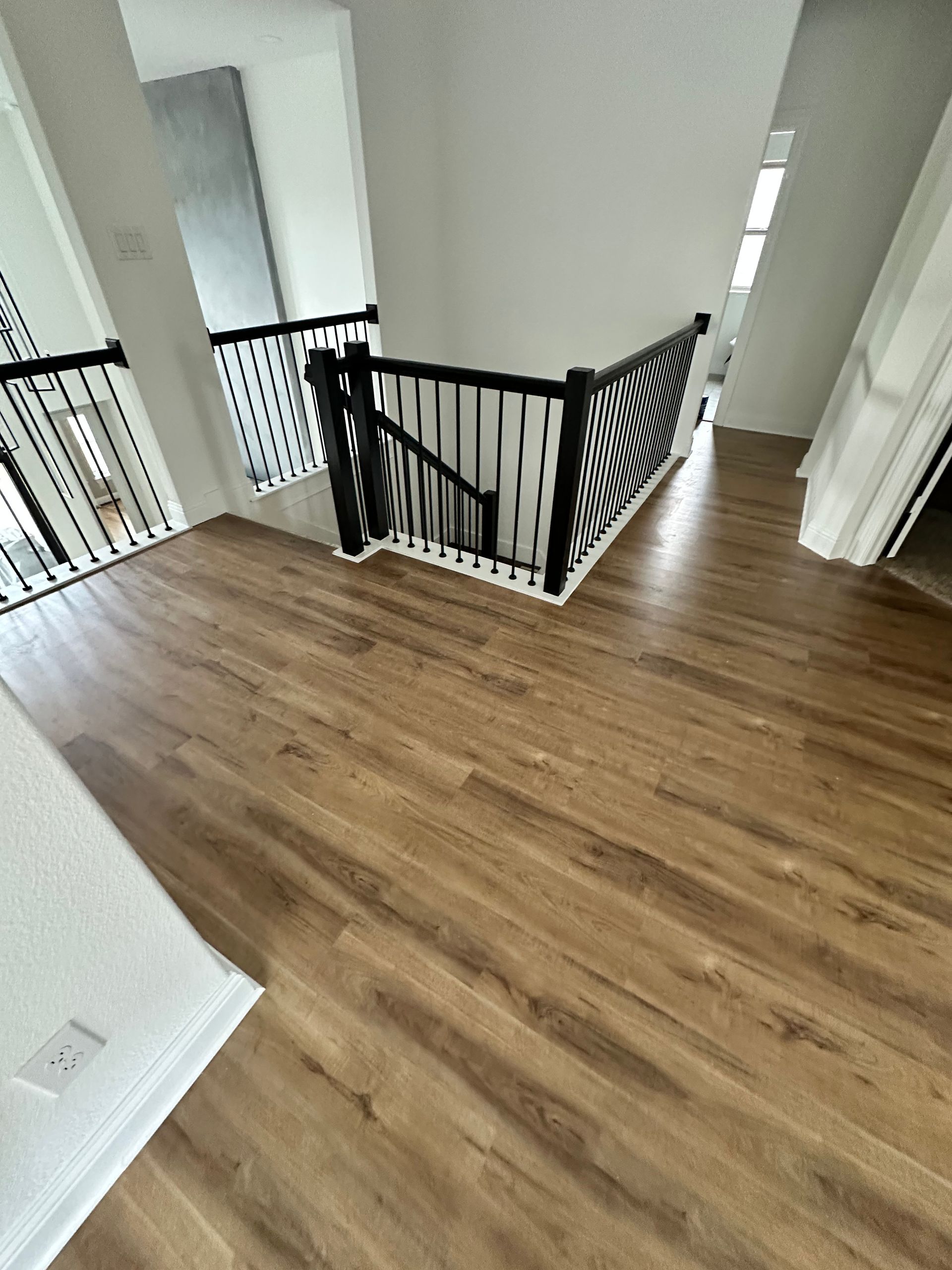 Brown wood flooring in a hallway with stairs and black railing, white walls.