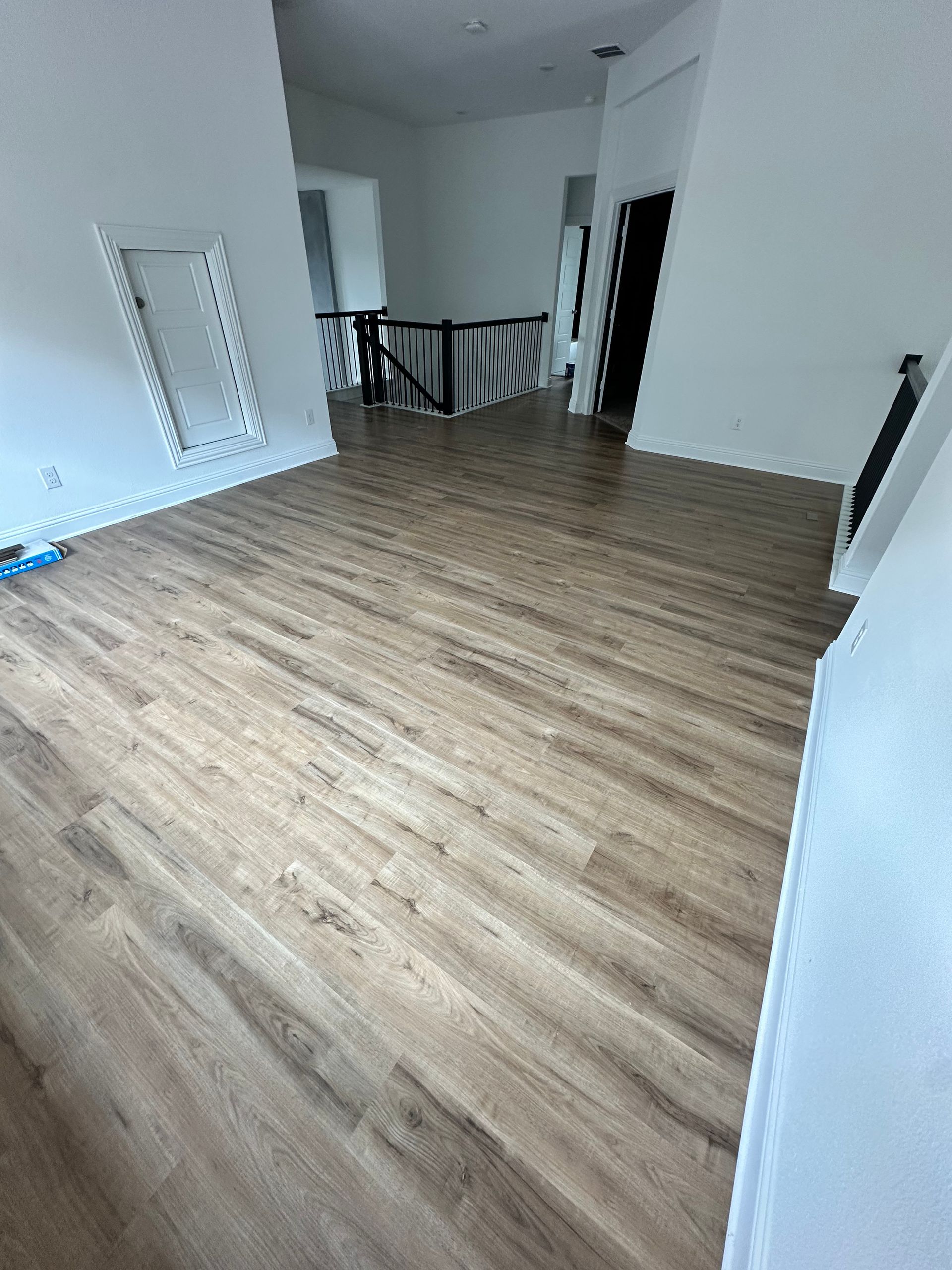 Light wood-look floor in a hallway, white walls, and a view to a balcony with dark railing.
