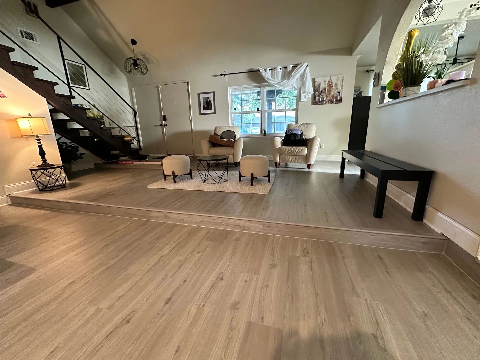 Living room with wood-look floors, staircase, seating area with chairs, and a bench along a wall.