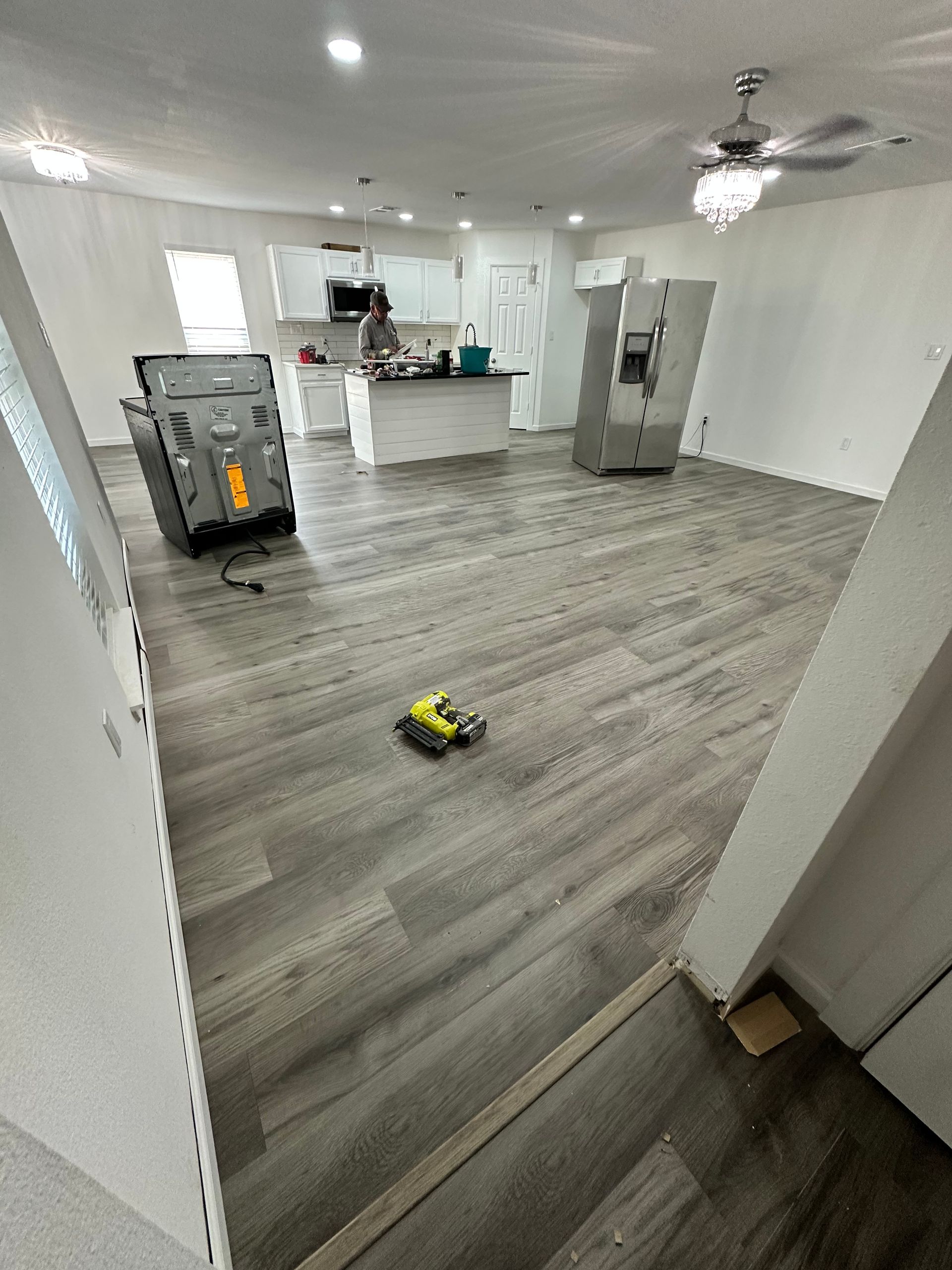 Open-concept room with new gray flooring, a kitchen island, and appliances. Construction in progress.
