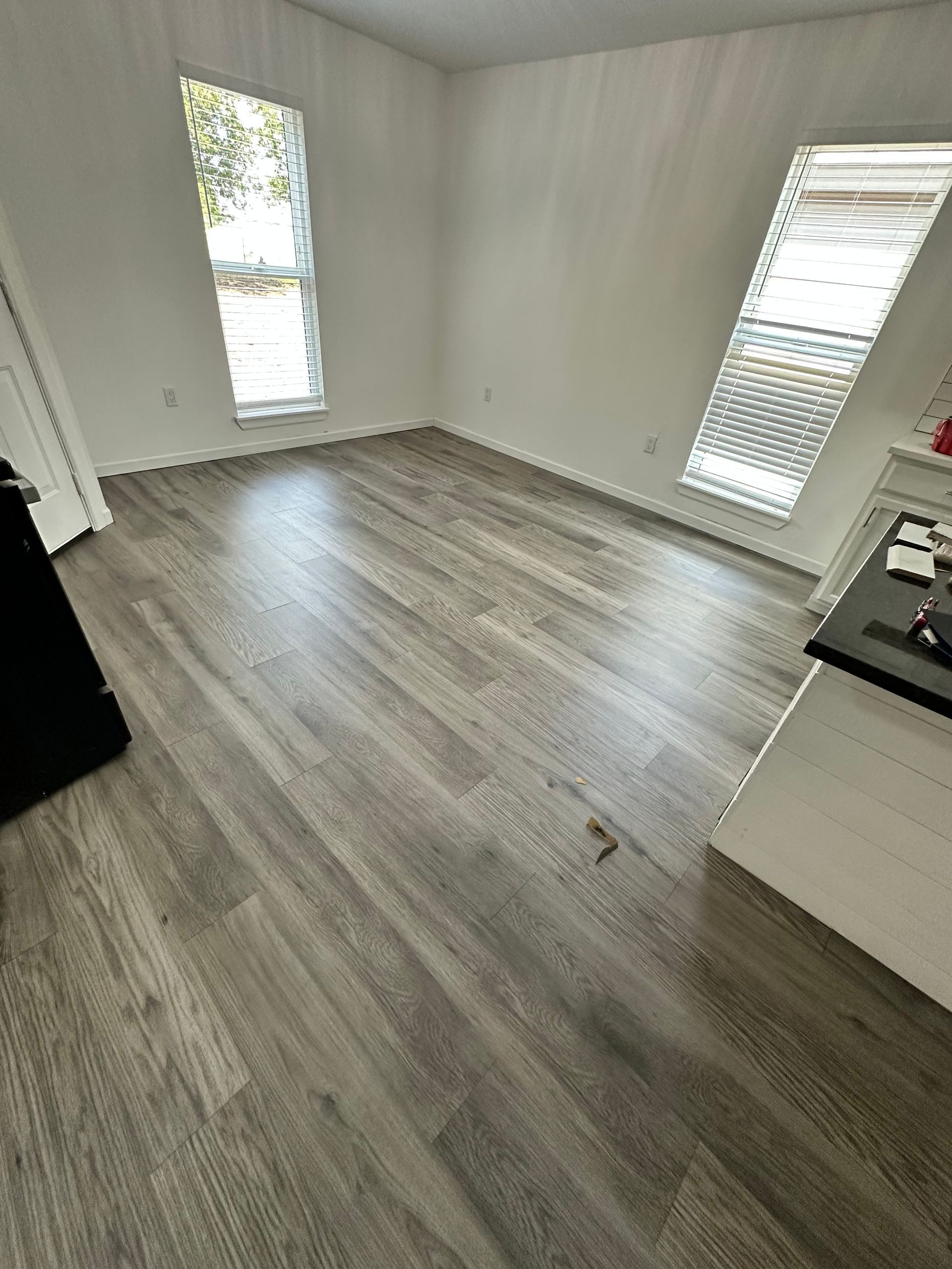 Empty room with gray wood-look flooring, white walls, and two windows.