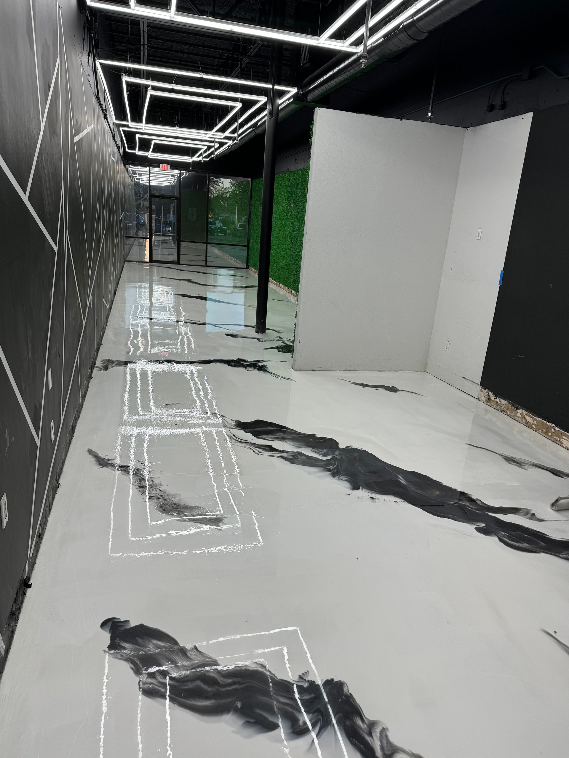 Long hallway with black and white design. White floor with black ink splotches, fluorescent lights.