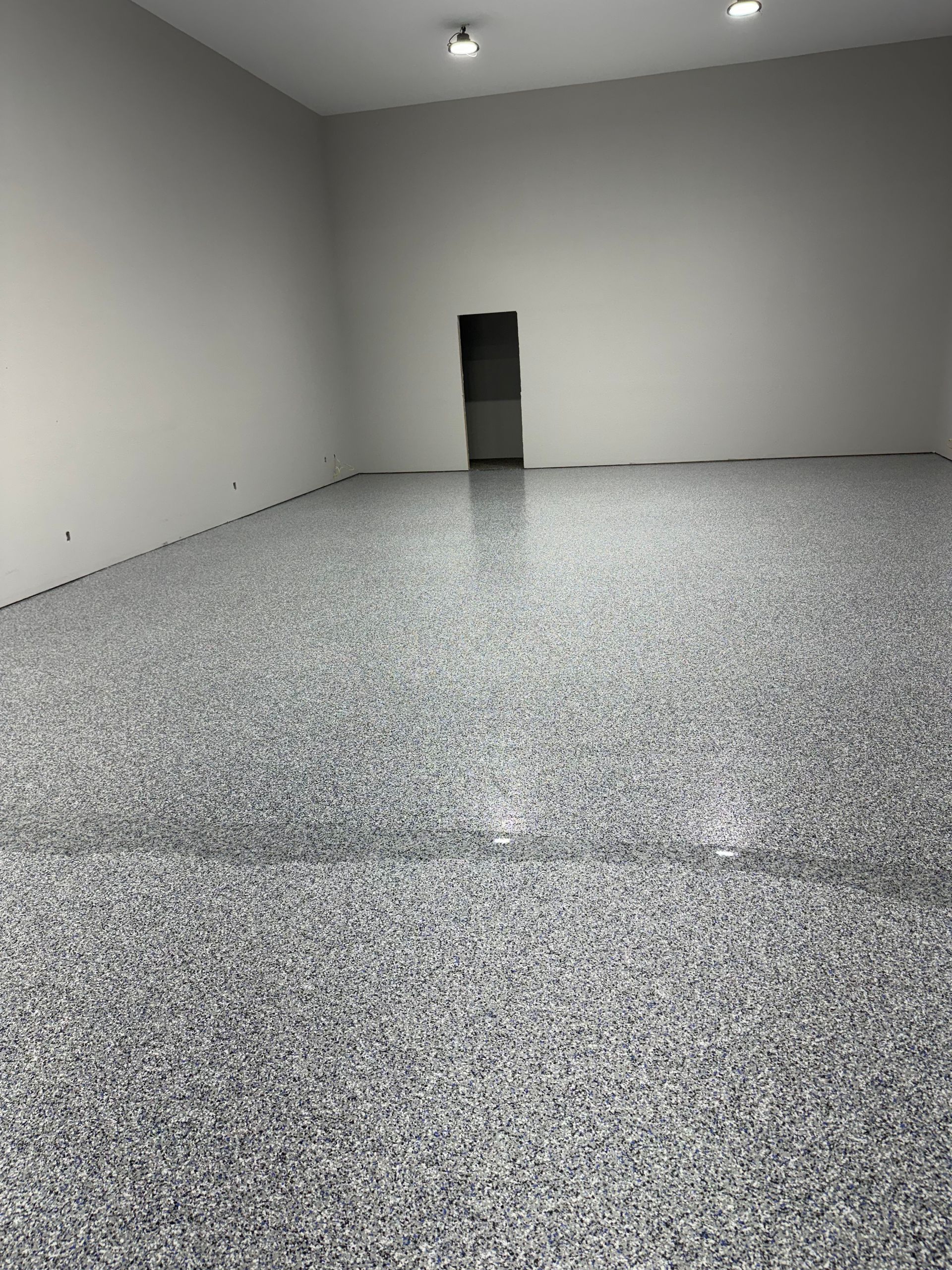 Empty garage with a speckled gray floor, white walls, and a doorway.