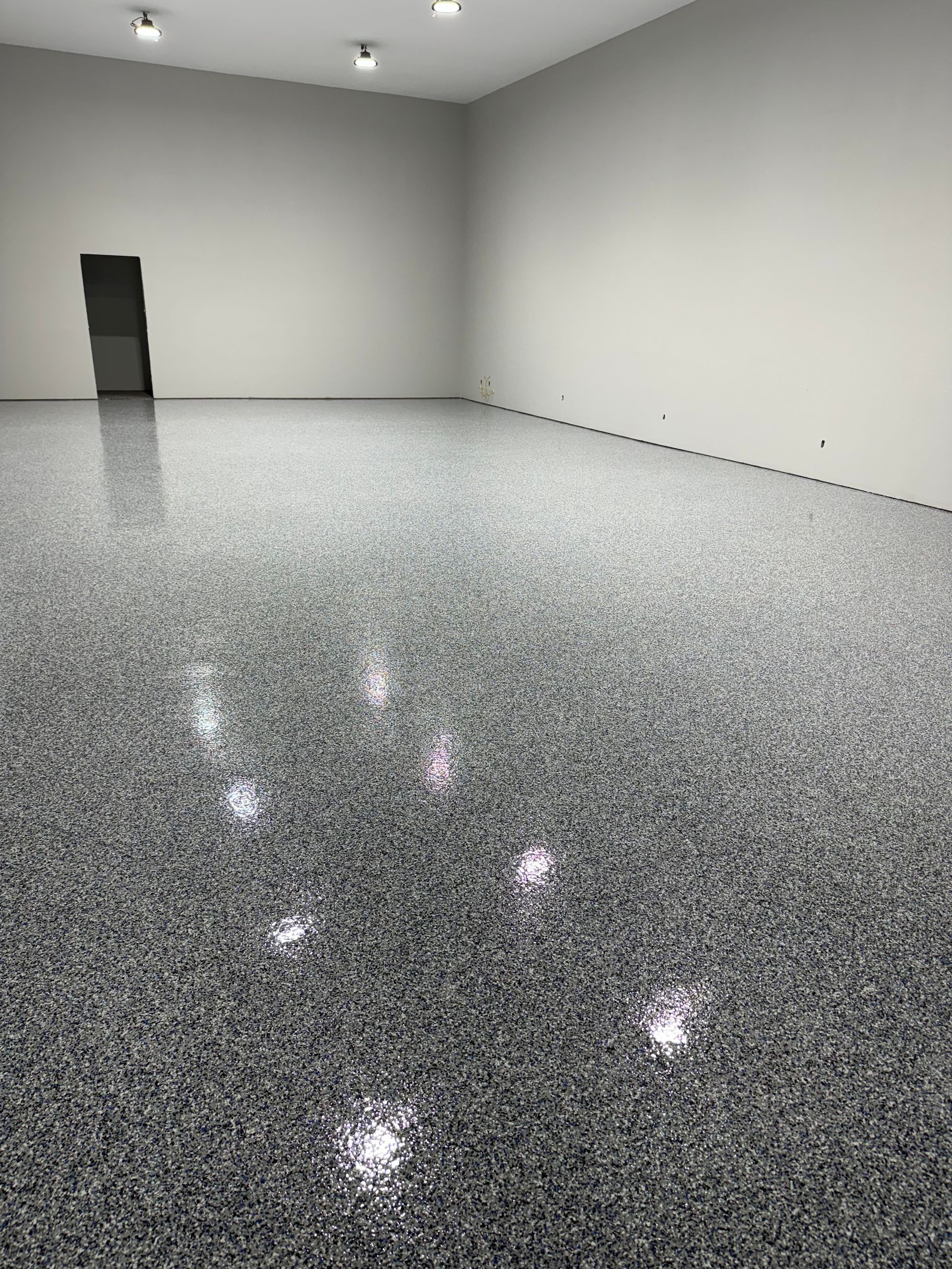 Empty room with a speckled gray and white epoxy floor, white walls, and recessed lighting.