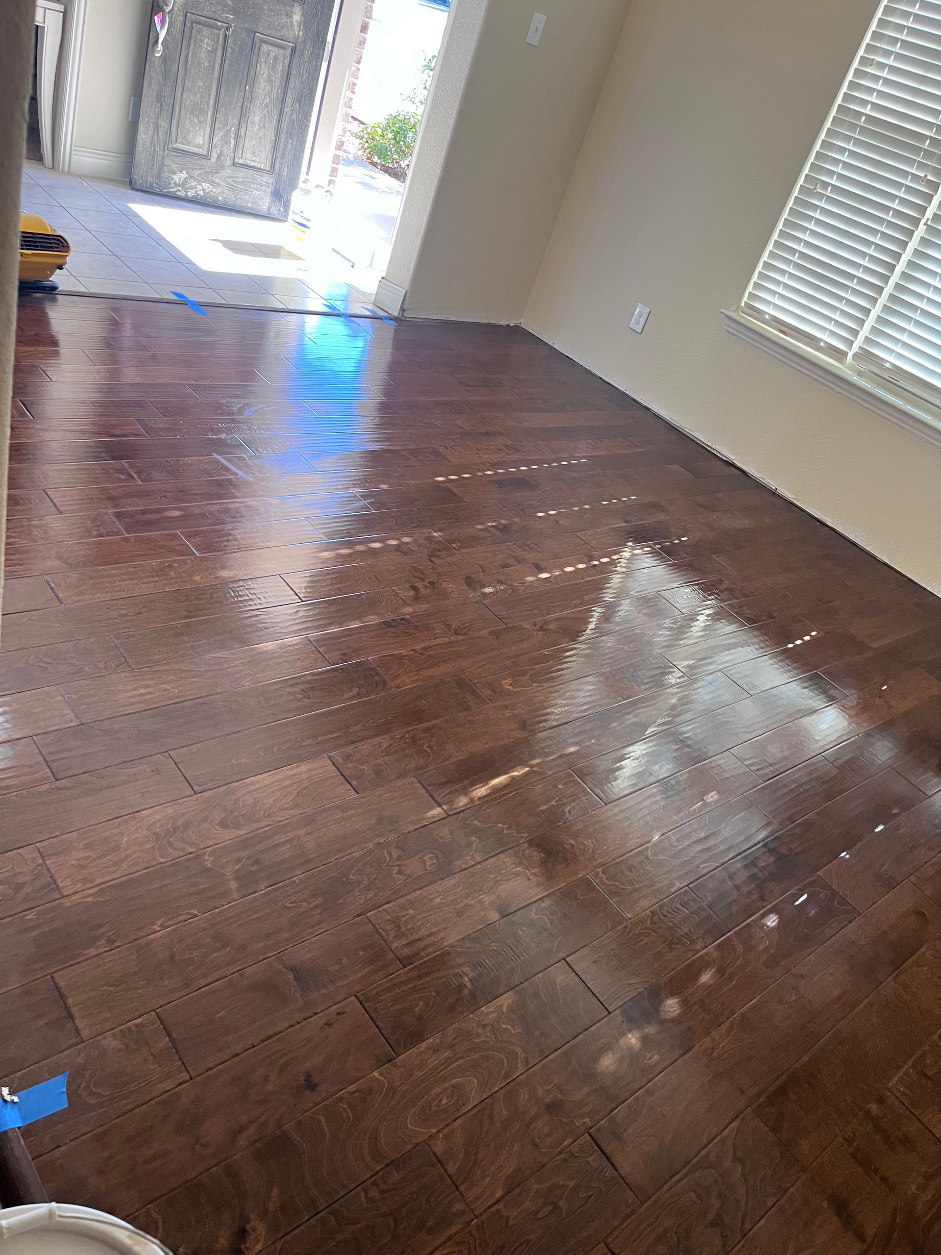 Brown hardwood floors with a shiny finish, likely after refinishing, in a well-lit room.