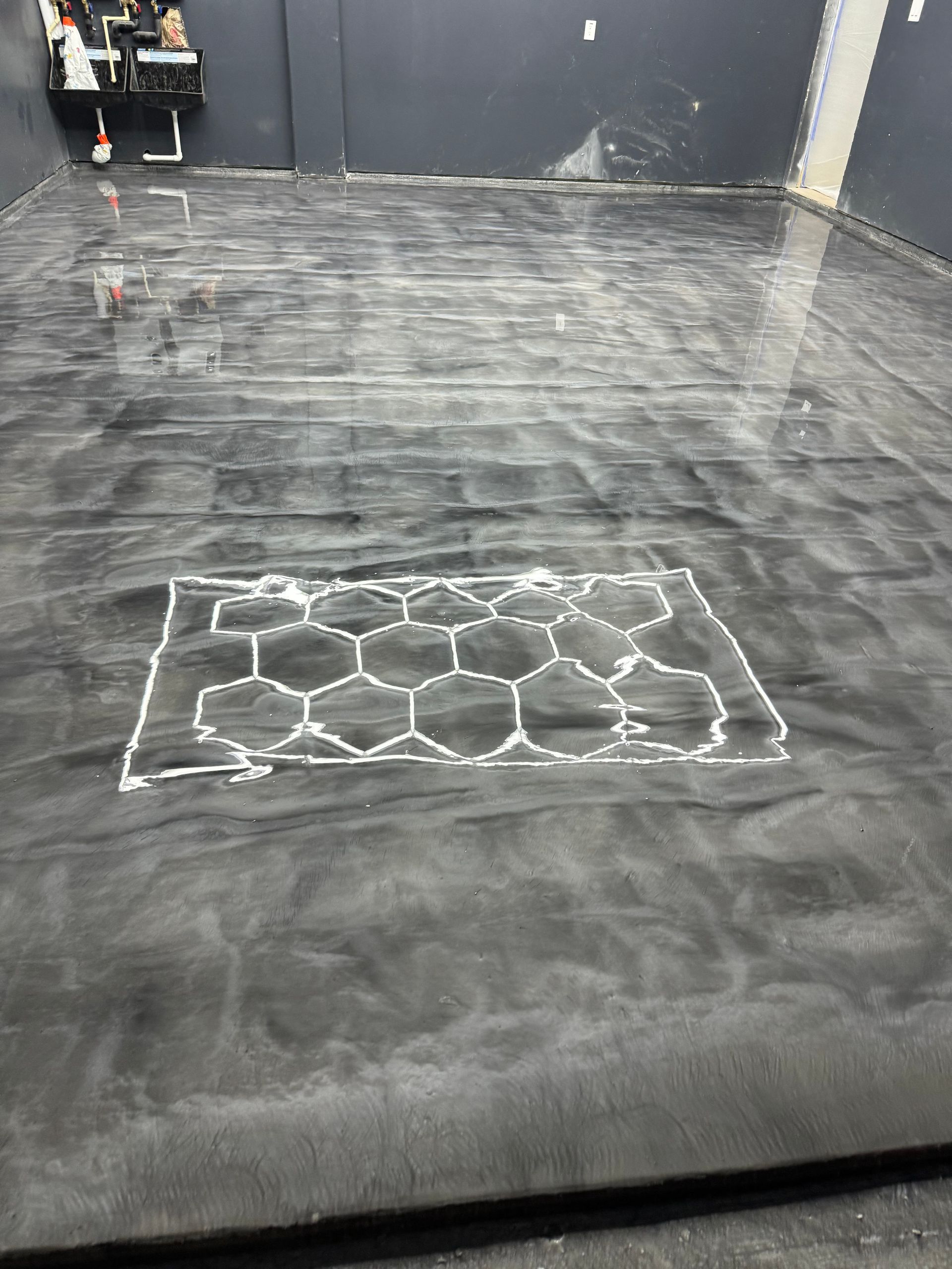 Gray epoxy floor with white hexagonal design drawn on it. Dark gray walls, construction setting.