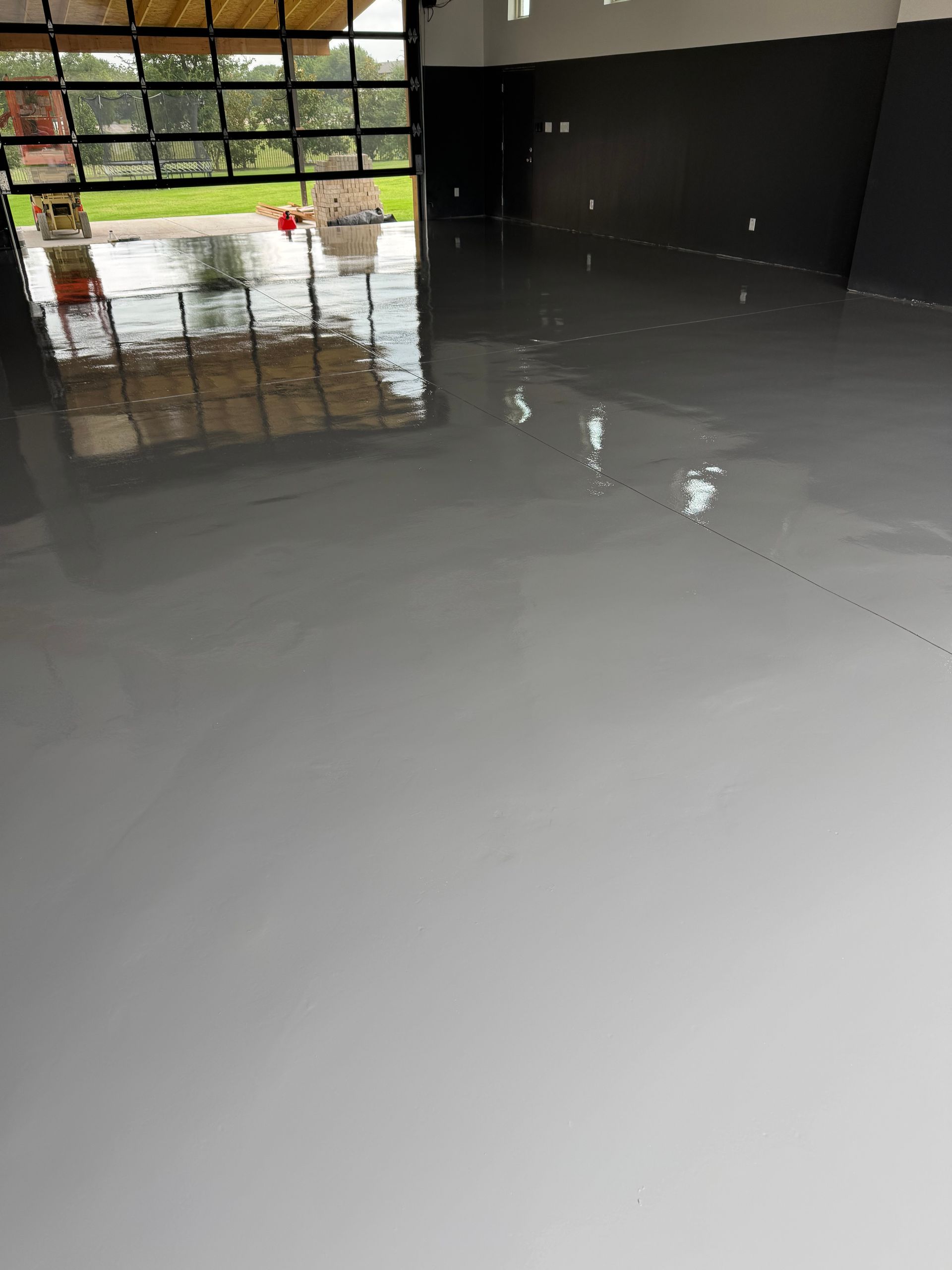Gray epoxy-coated garage floor reflects the interior and exterior; black wall.