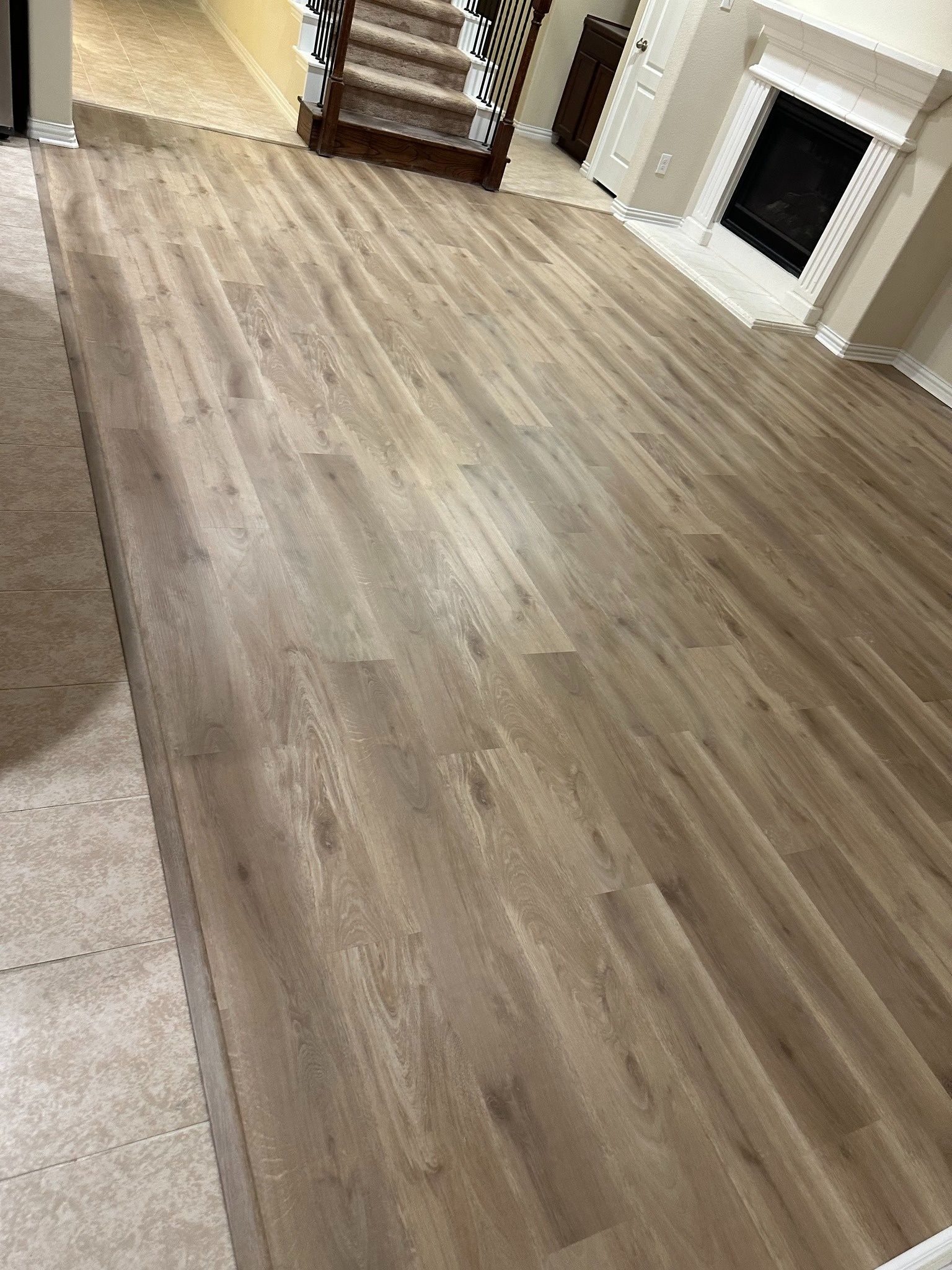 Wooden-look flooring in a living room with stairs in the background and a fireplace.