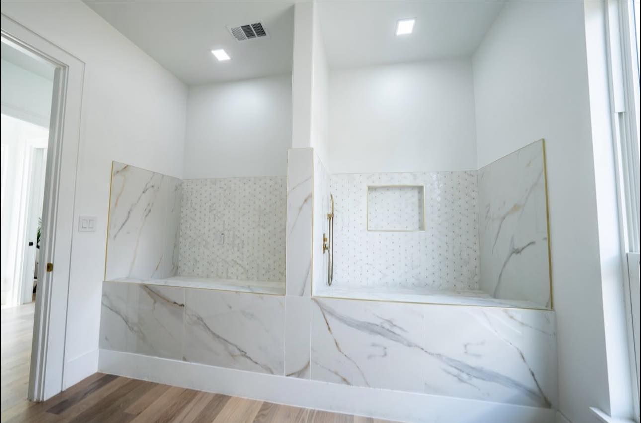Two showers with marble-like tile, benches, and recessed niches in a bright white bathroom.