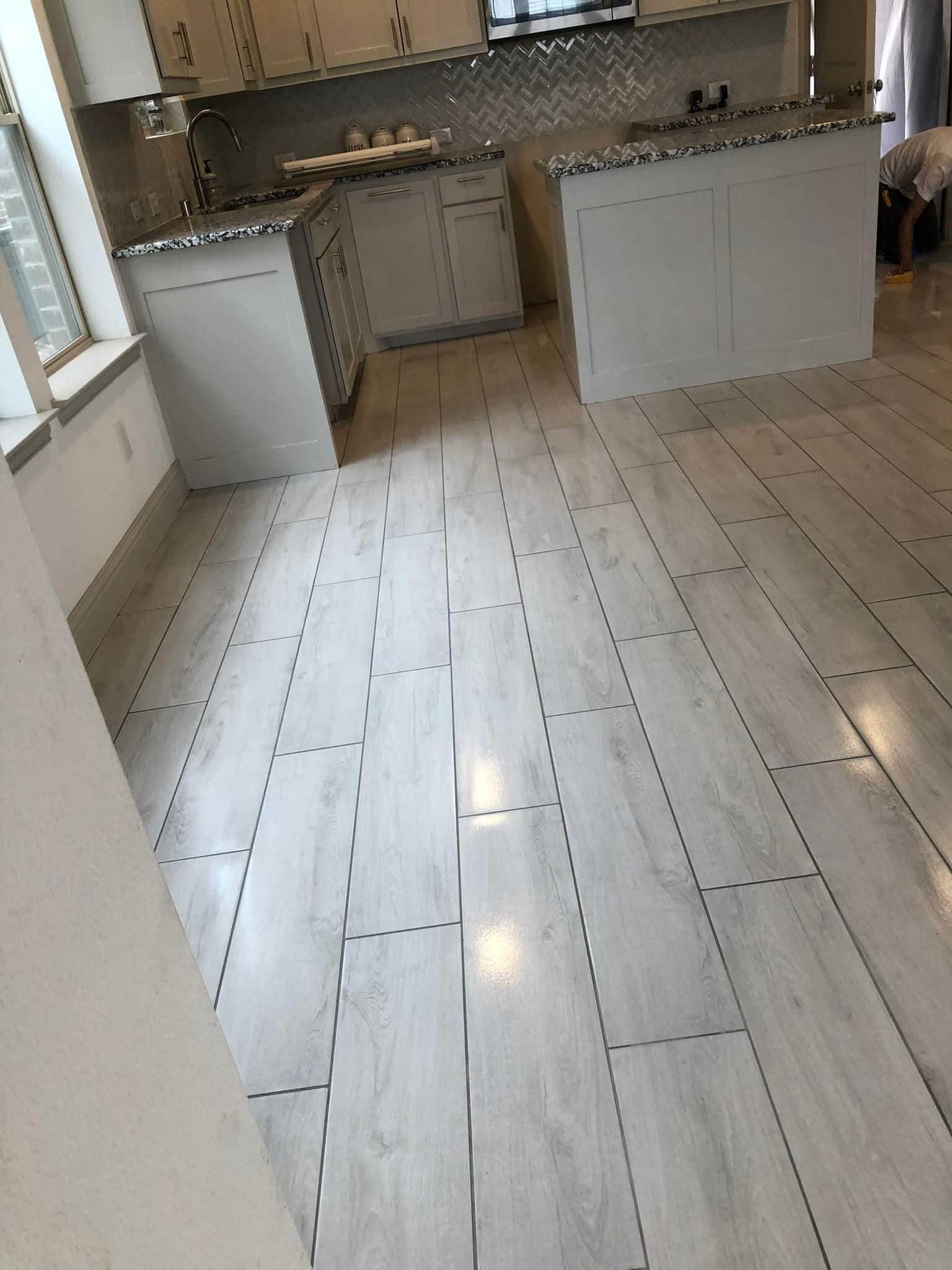 Light gray wood-look tiled floor in a kitchen with white cabinets and countertops.