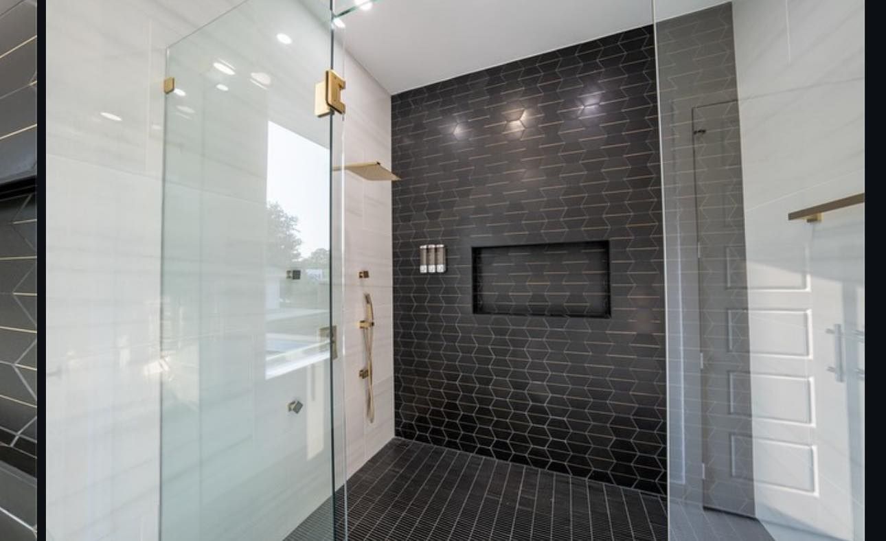 Modern bathroom with glass shower, black and white tile walls, gold fixtures.