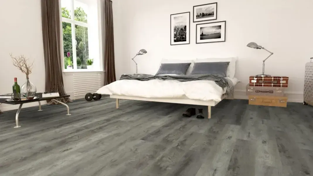 Bedroom with grey wood-look flooring, white walls, bed, and furniture; window with curtains on the left.