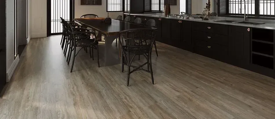 Wooden flooring in a modern kitchen with dark cabinetry and dining table with black chairs.
