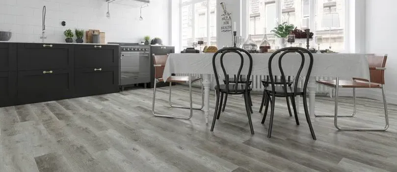 A bright kitchen with dark cabinets, a dining table, and wooden floorboards.